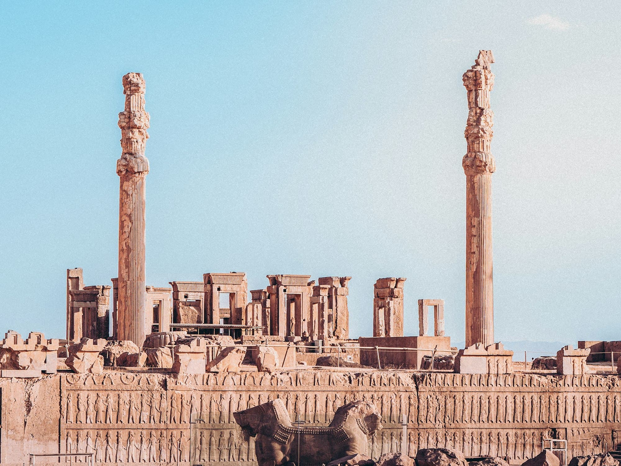 Tall stone columns and carved ruins of Persepolis under a pale sky