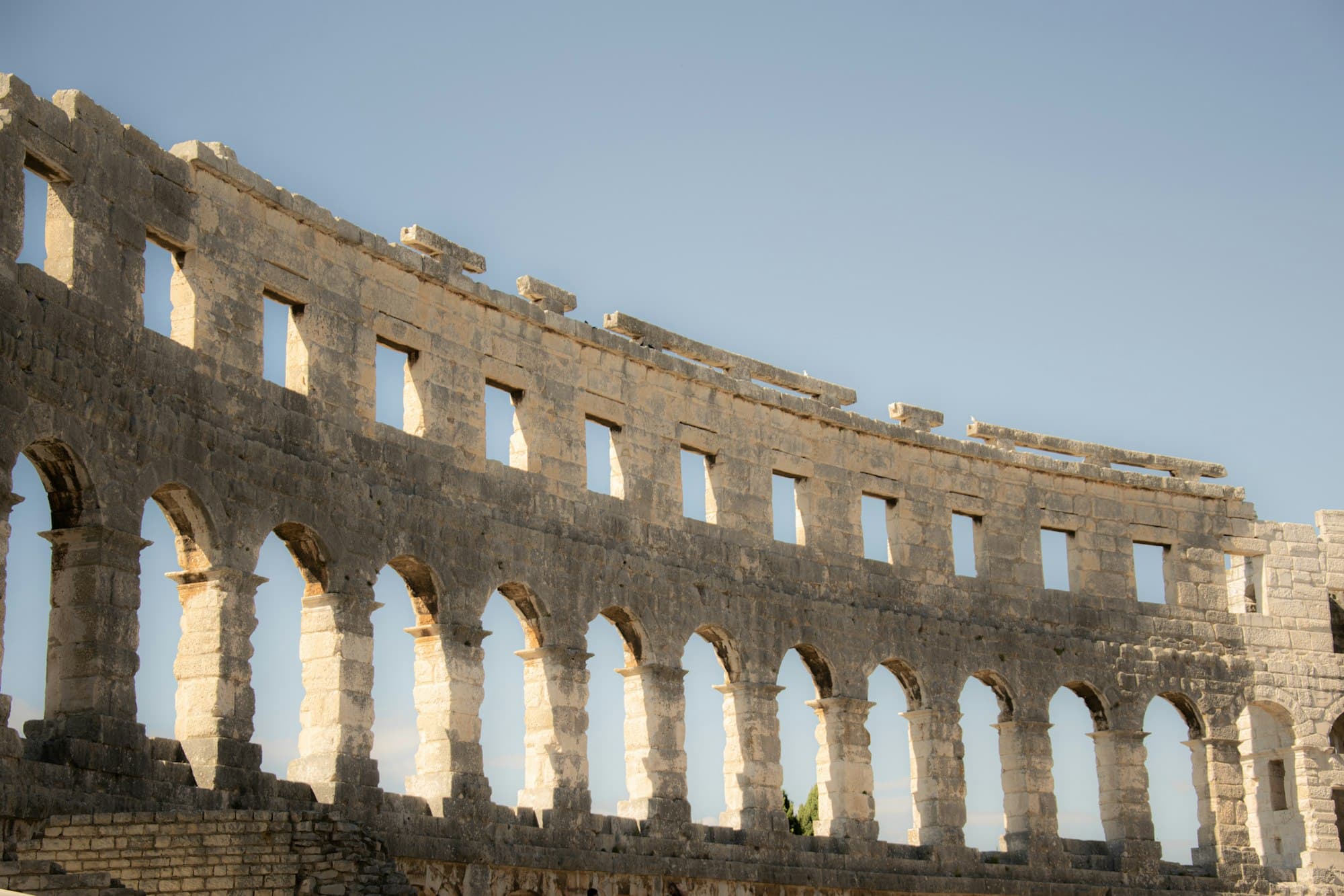 The weathered stone arches of the Roman amphitheatre in Pula against a blue sky