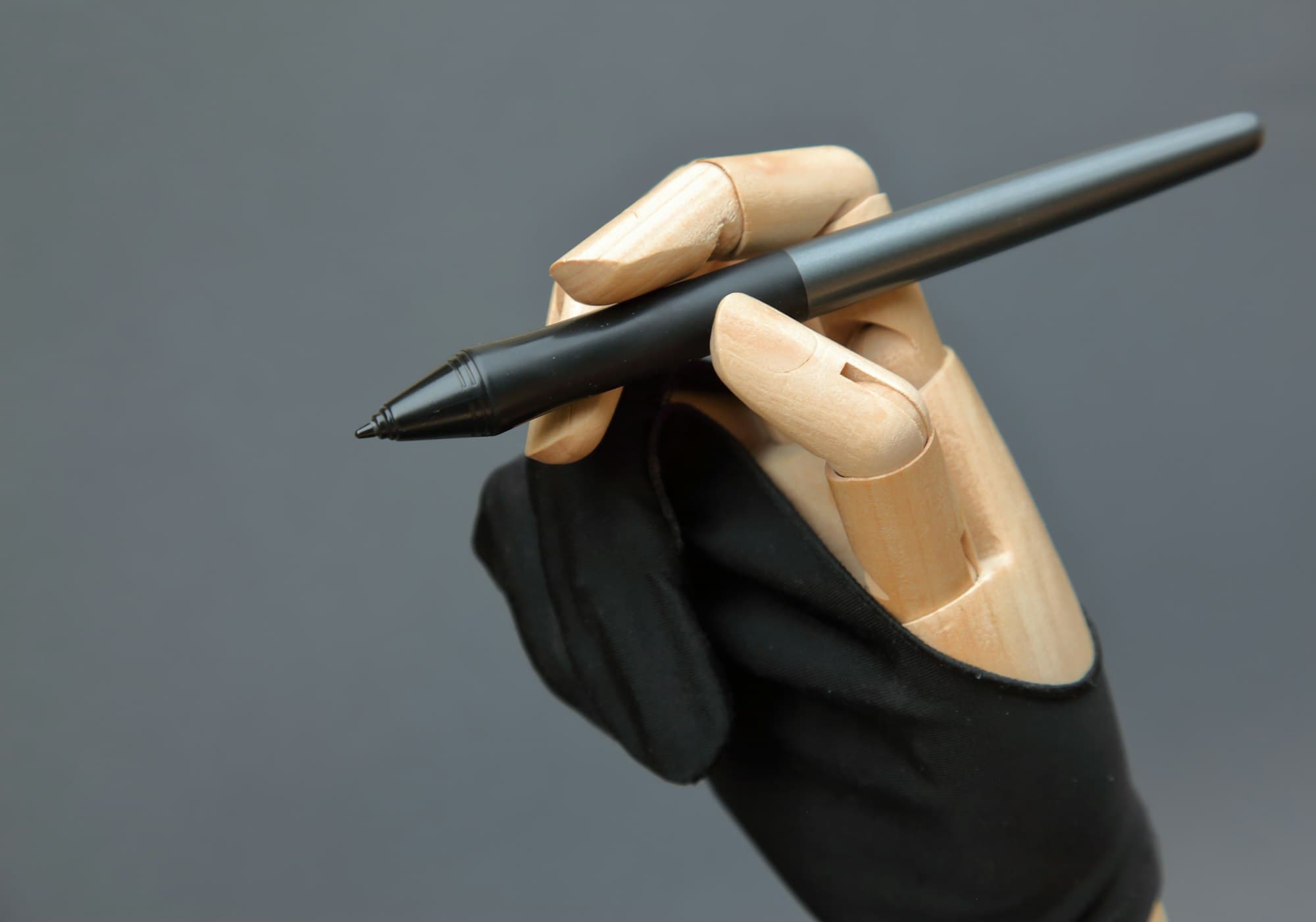 A wooden mannequin hand in a black artist glove holding a digital stylus
