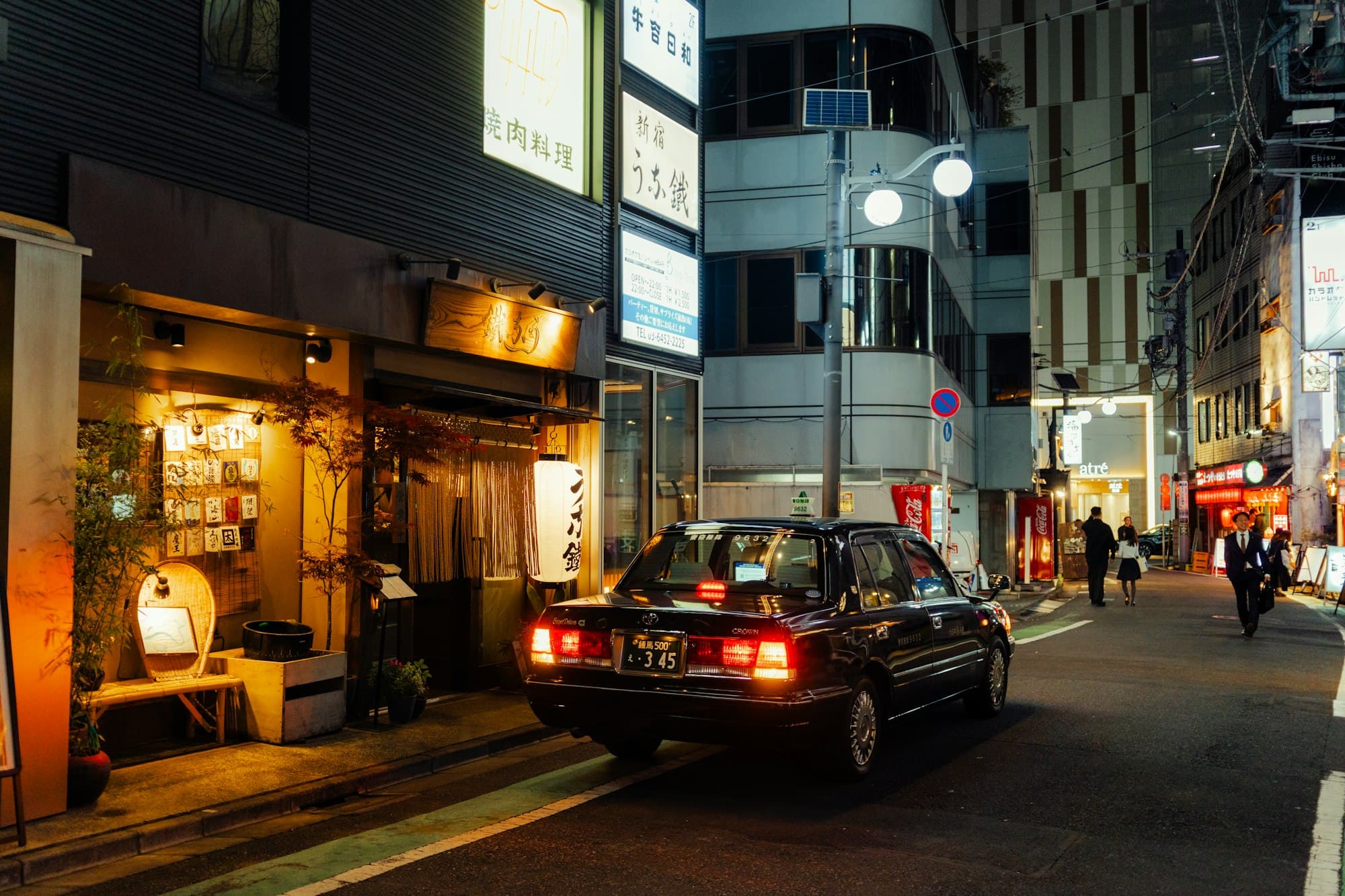 A black taxi parked on a narrow lantern-lit street in Tokyo at night