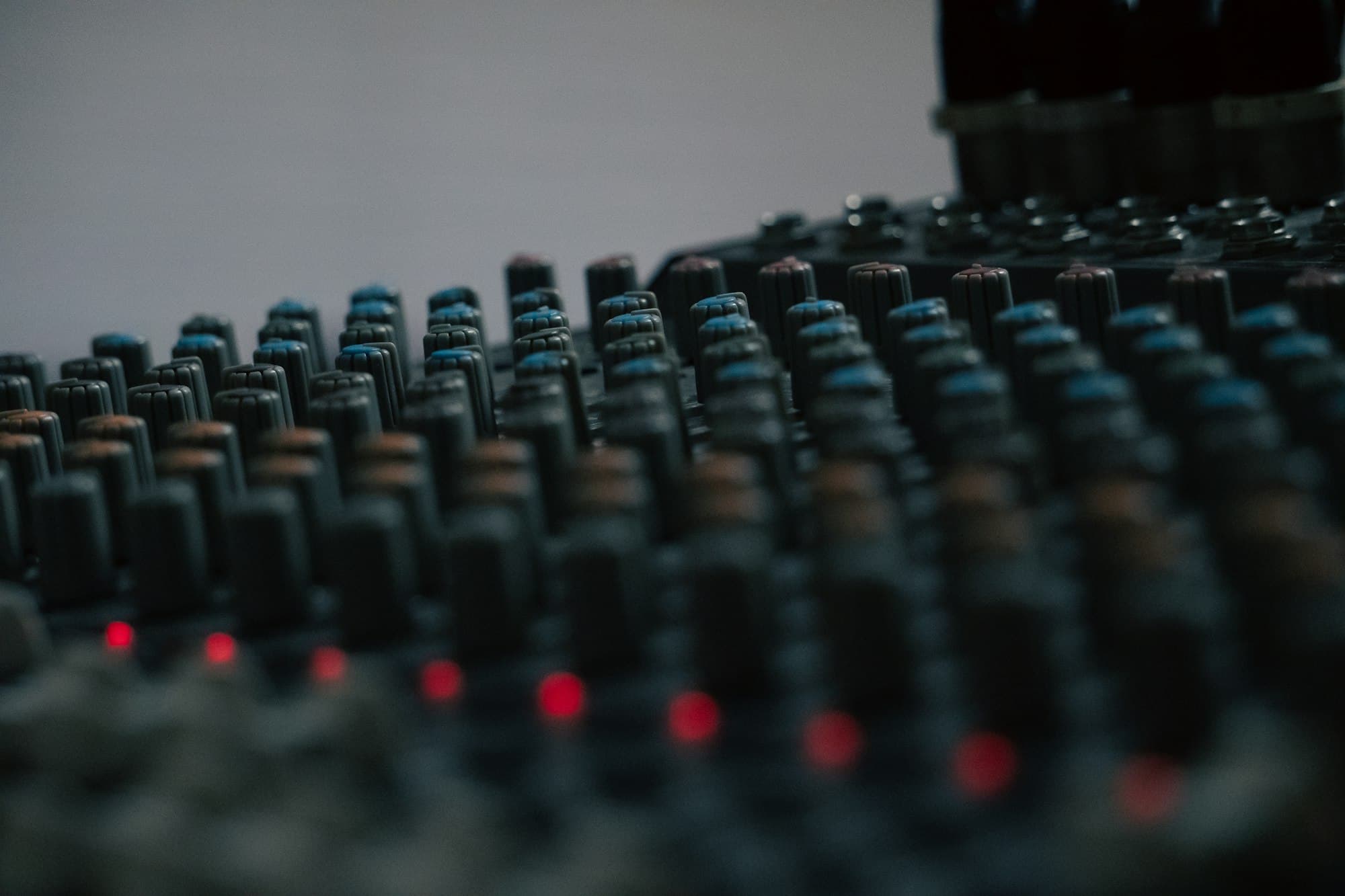 A studio mixing console with rows of knobs and glowing red lights