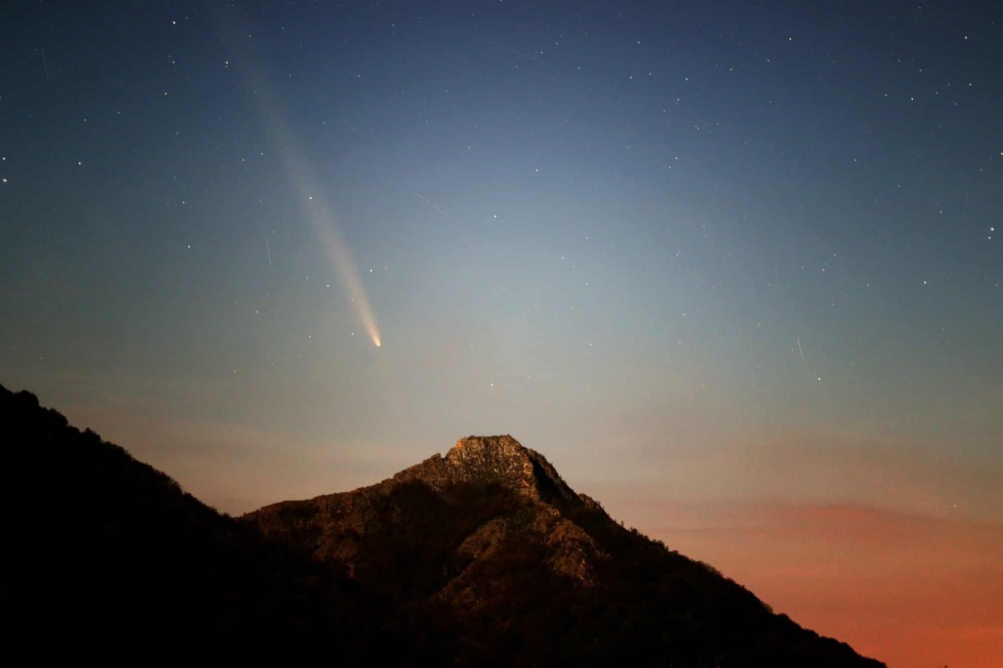 A bright comet with a long tail above a dark mountain peak at twilight
