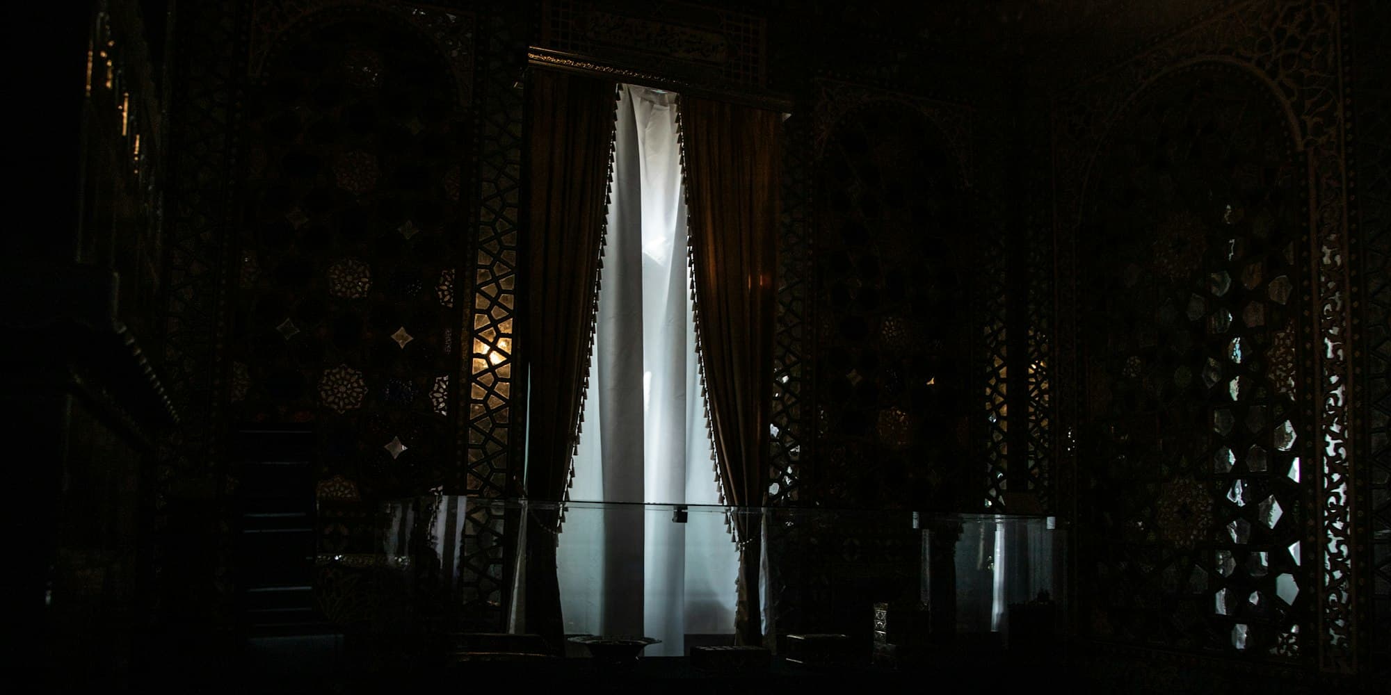 Bright light through draped curtains in a dark room with ornate latticed walls