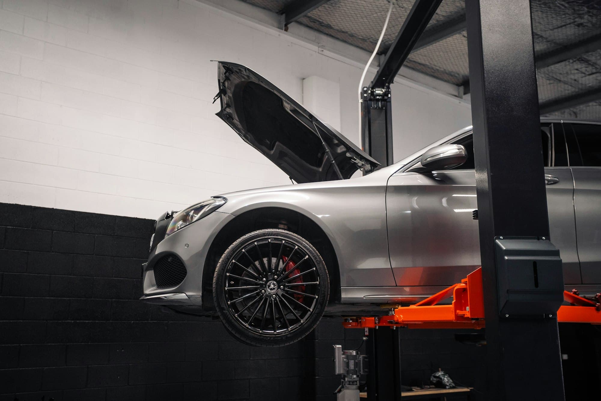 A silver car with its hood open on an orange lift in a workshop