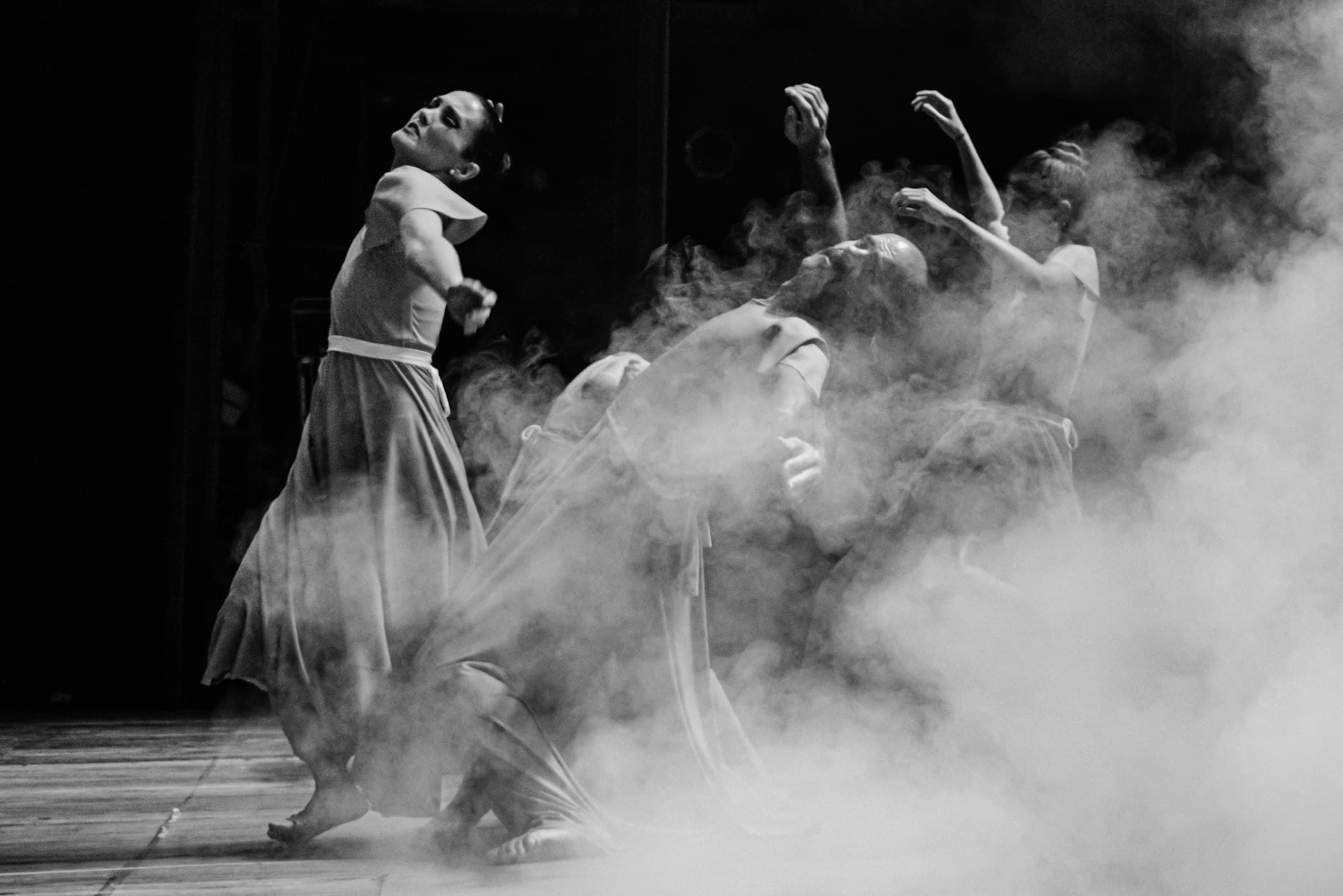 Dancers in flowing dresses performing on a dark stage filled with smoke