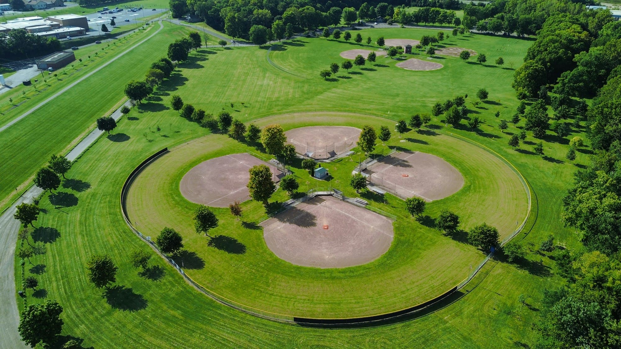 An aerial view of four baseball diamonds in a cloverleaf pattern among green lawns and trees