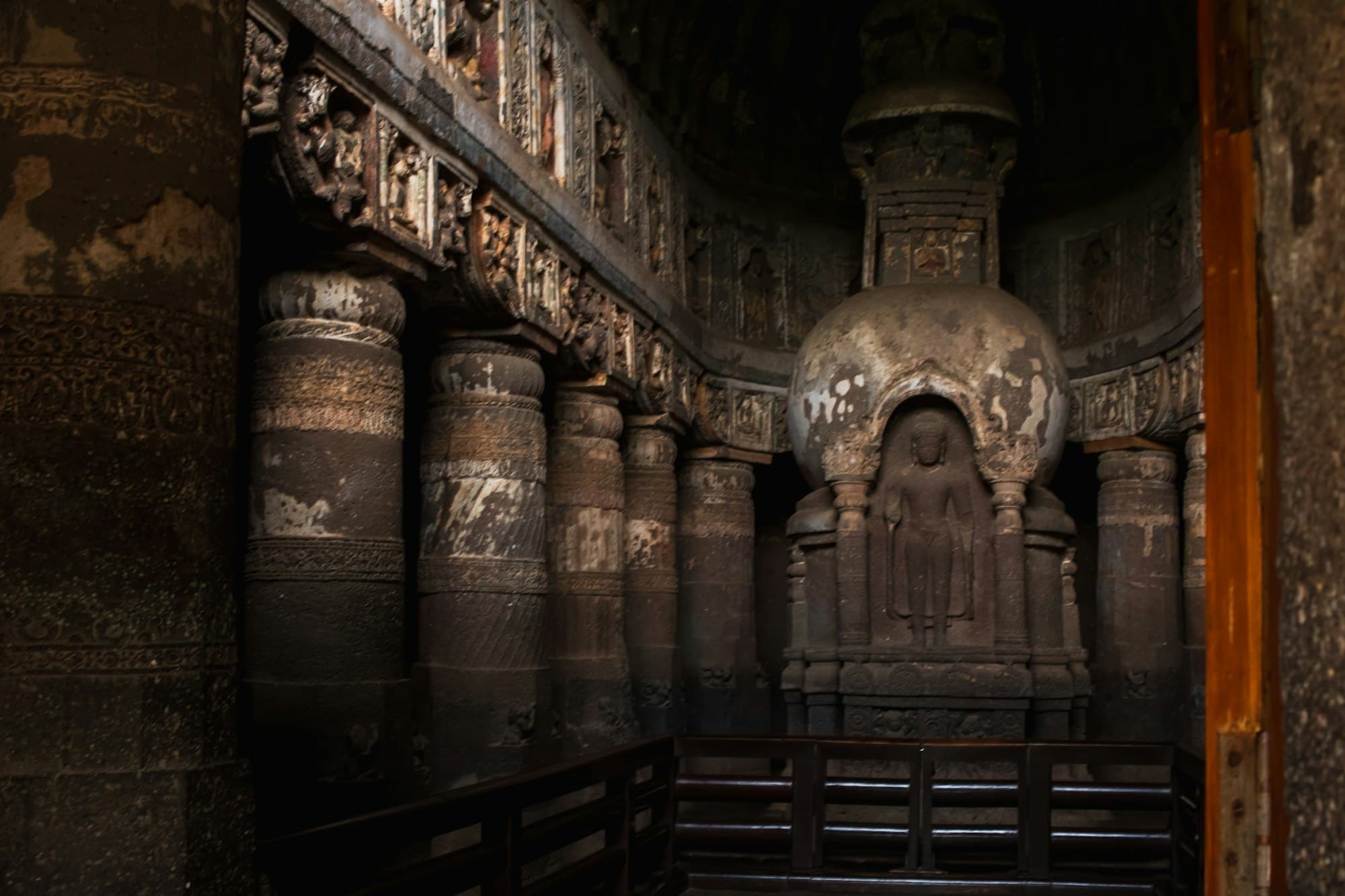 A carved stone stupa with a Buddha figure and ornate columns inside the Ajanta Caves
