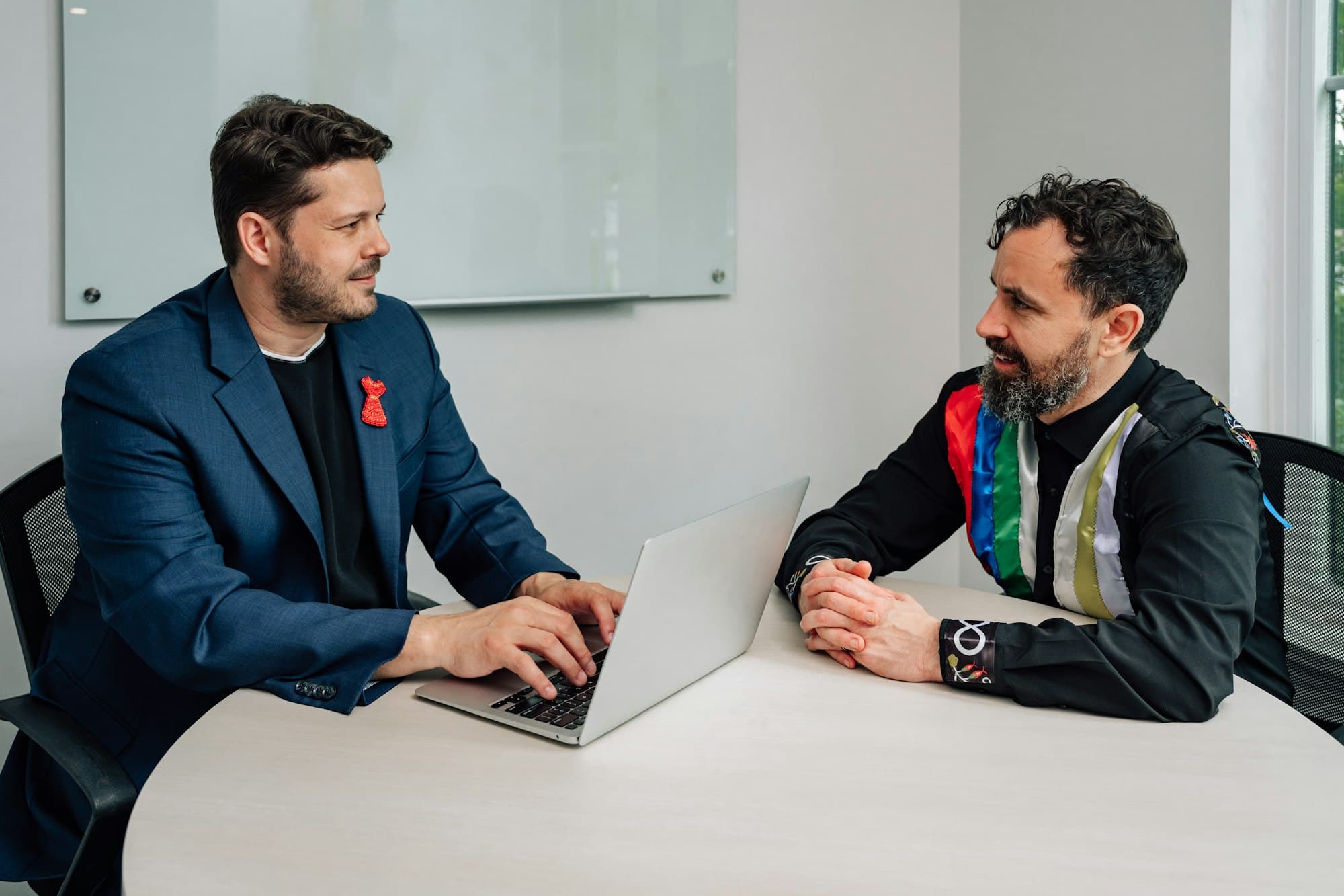 Two men talking across a round table with a laptop in a bright office