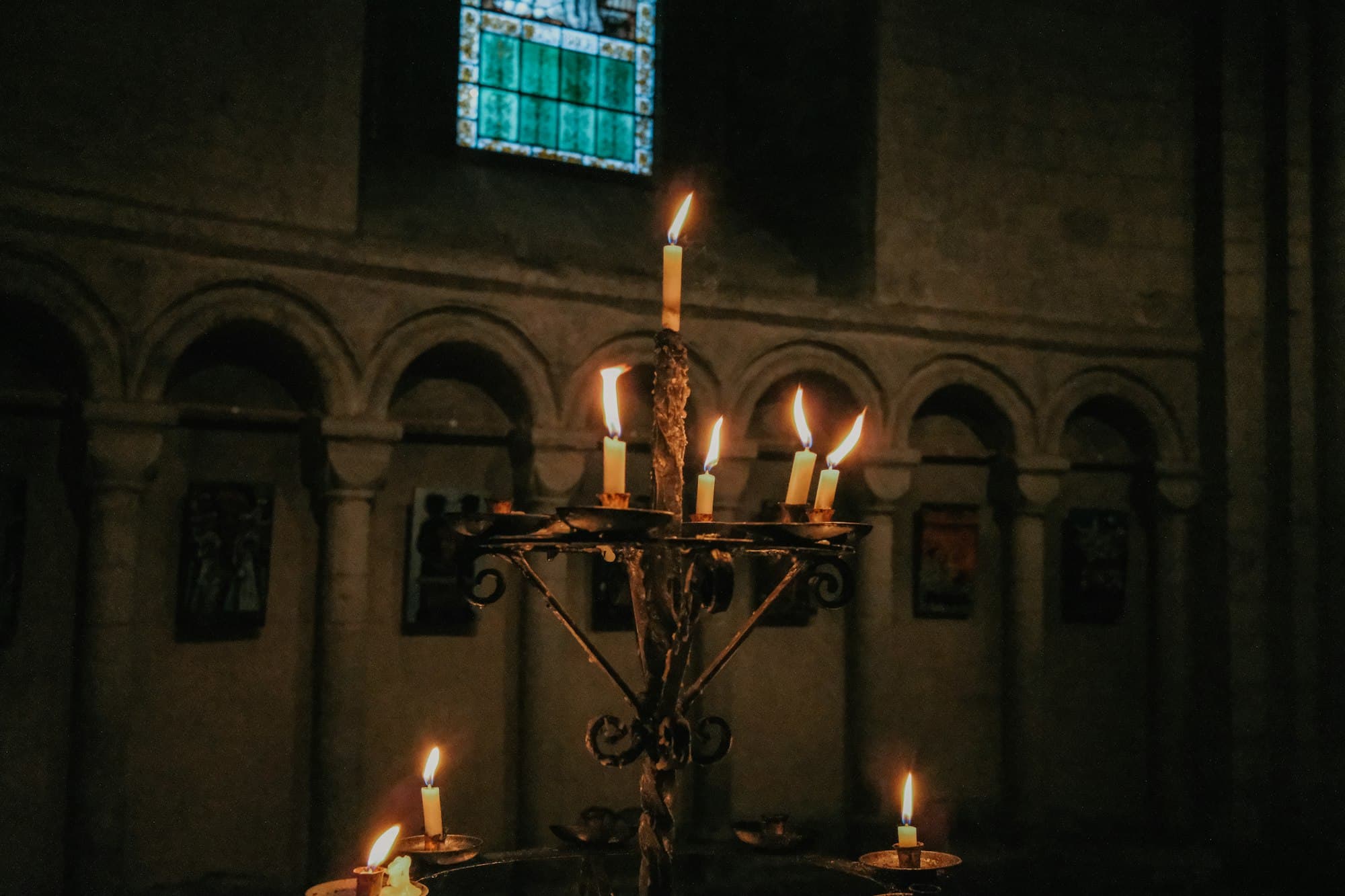 Lit candles on a wrought iron stand in a dimly lit stone church