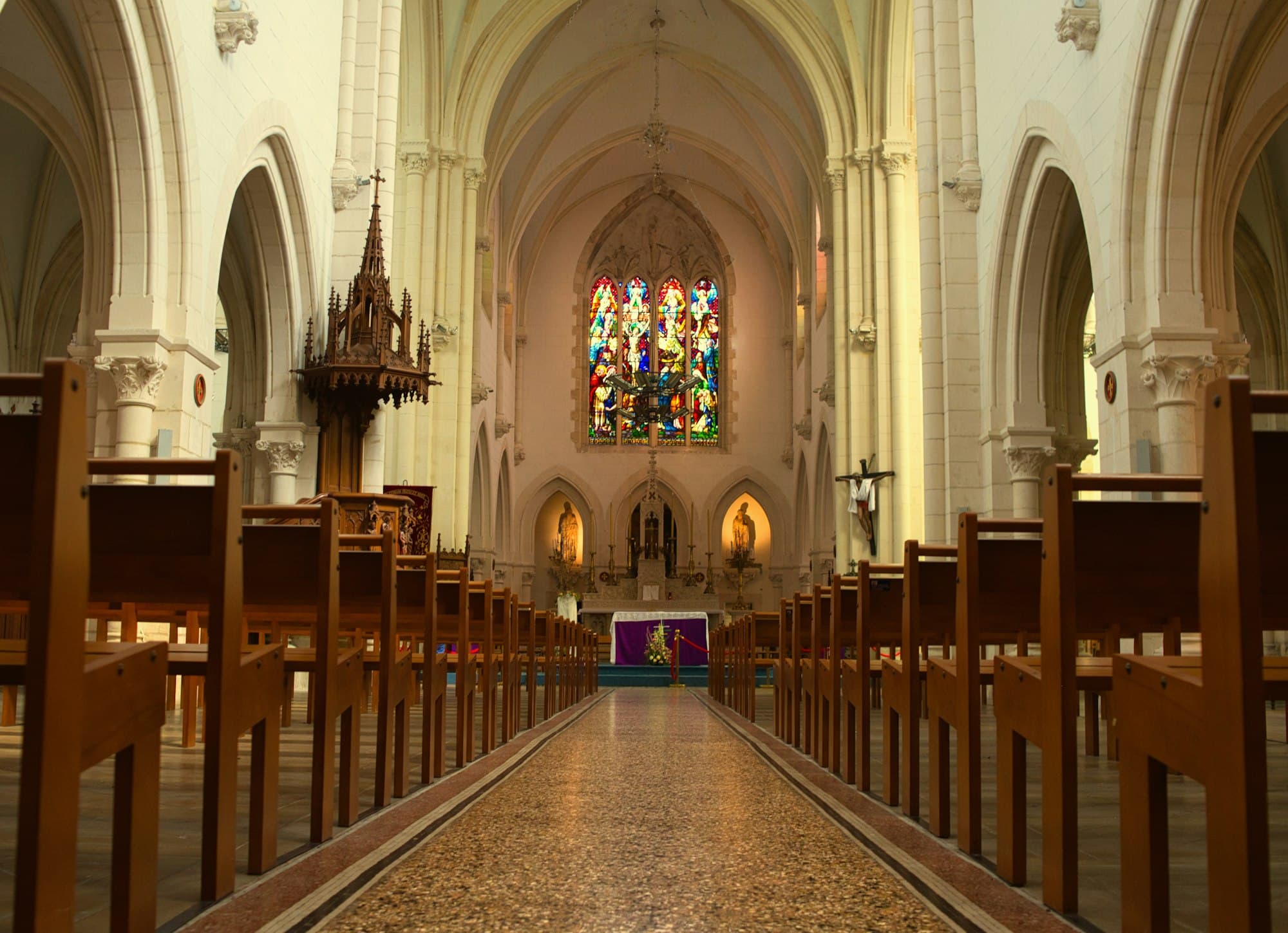A long church aisle between wooden pews leading to a stained glass window