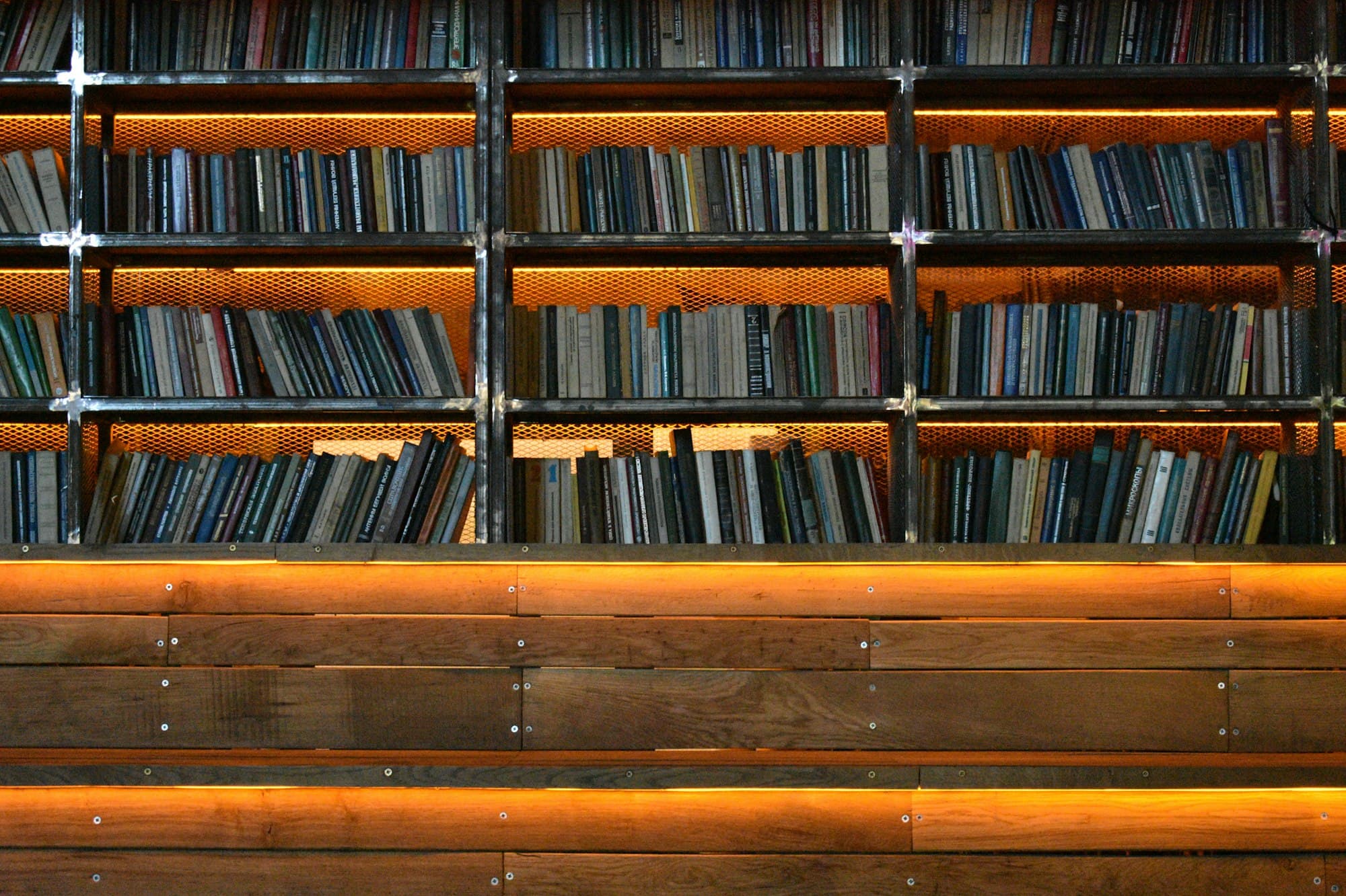 Rows of books on metal shelves above warm orange backlit wooden panels