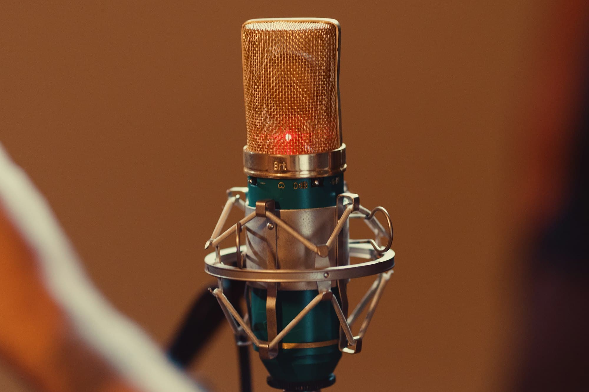 A vintage condenser microphone with a glowing red on-air light against a warm brown background