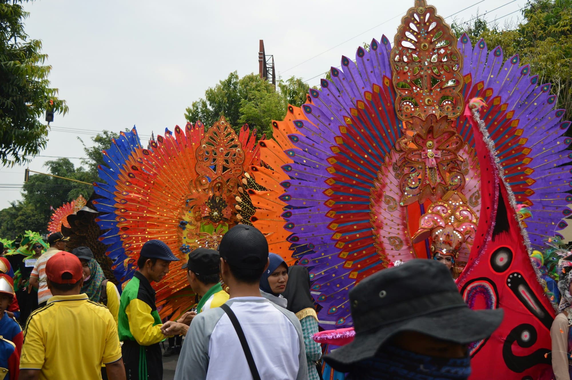 People gathered at a street parade beside large colourful feathered costumes