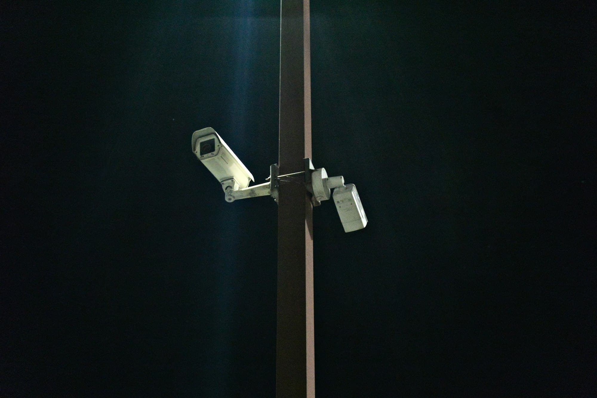 Two security cameras mounted on a tall pole against a dark night sky