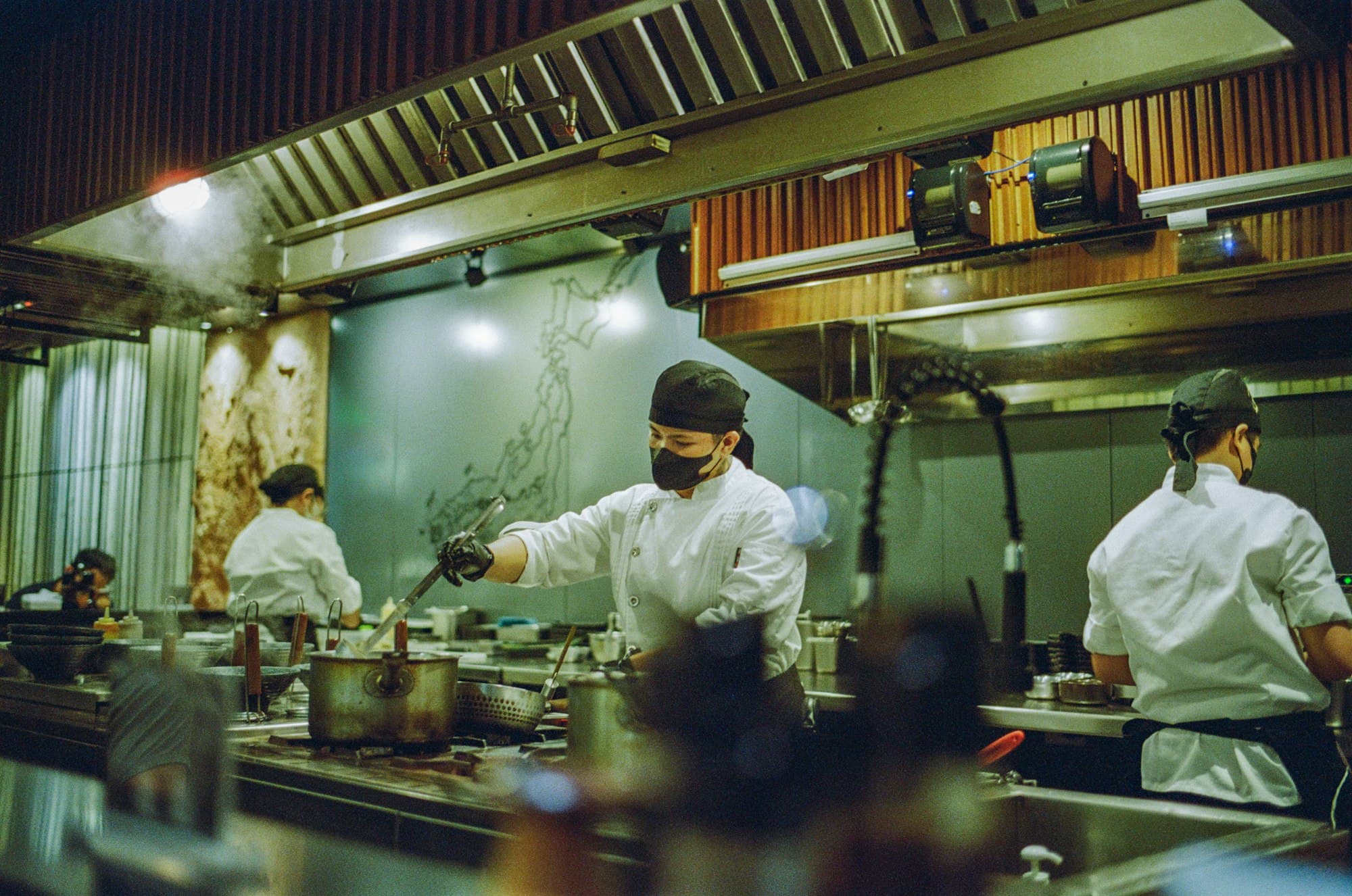 Chefs in white jackets cook at the stoves of a busy restaurant kitchen