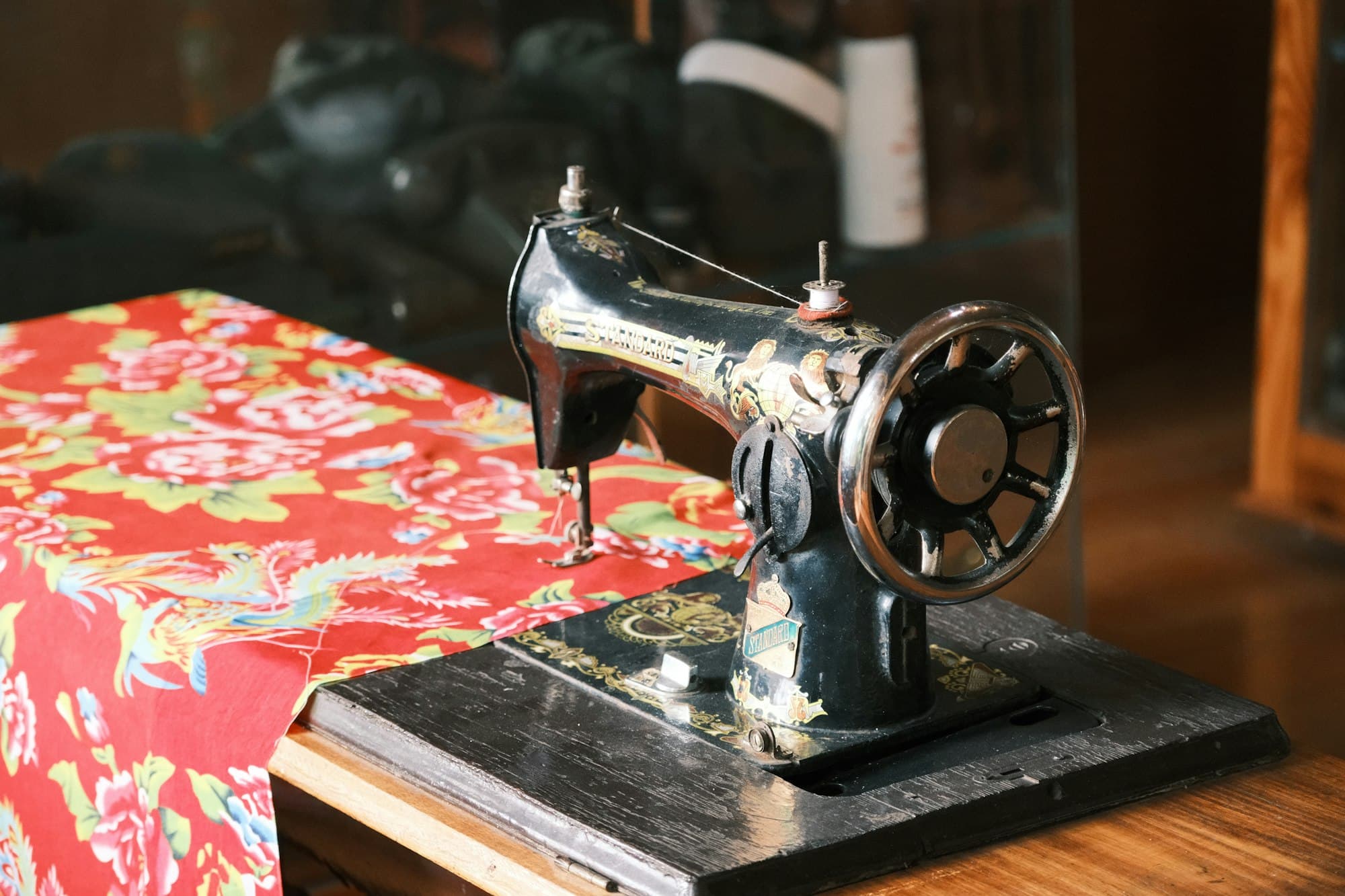 A vintage black sewing machine on a wooden table beside red floral fabric