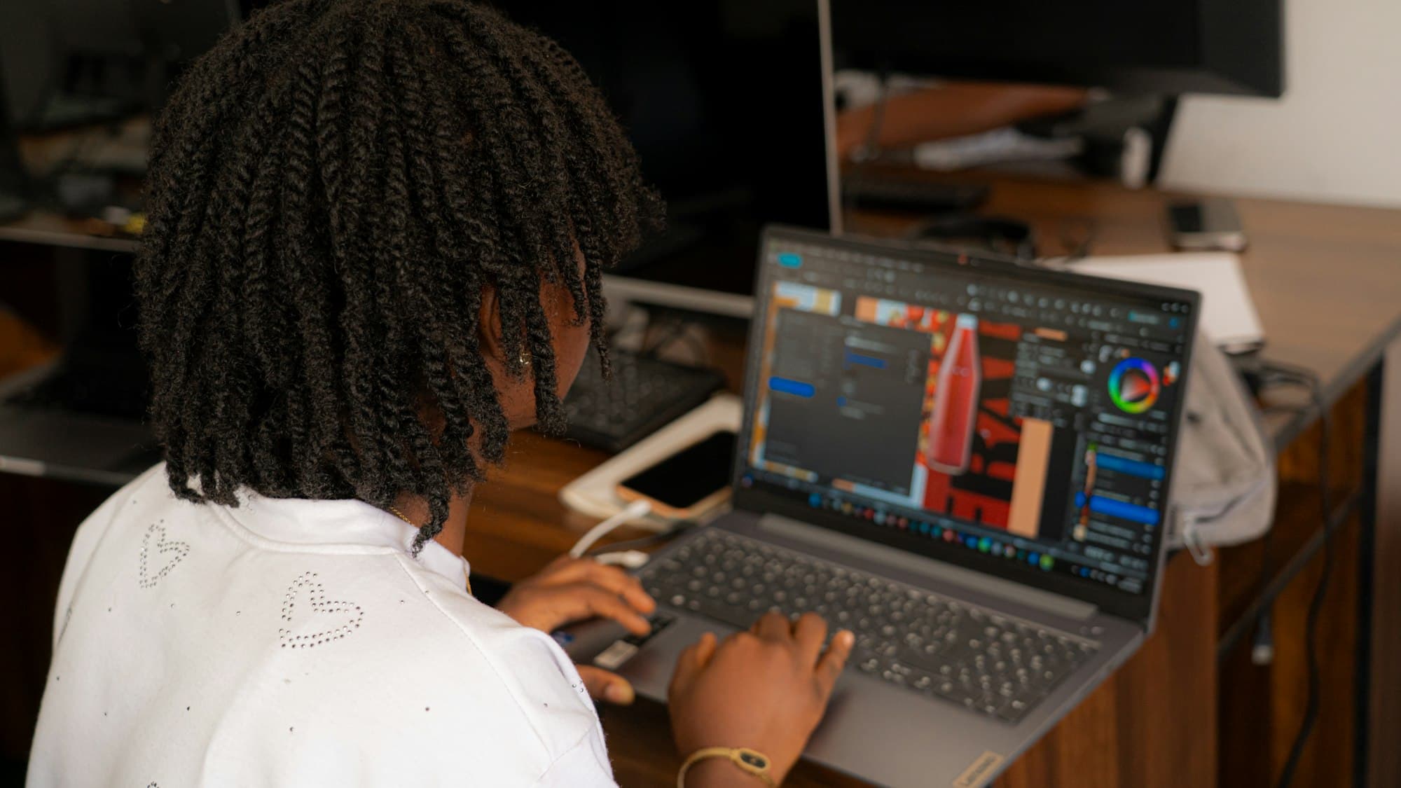 A designer seen from behind working in design software on a laptop at a wooden desk