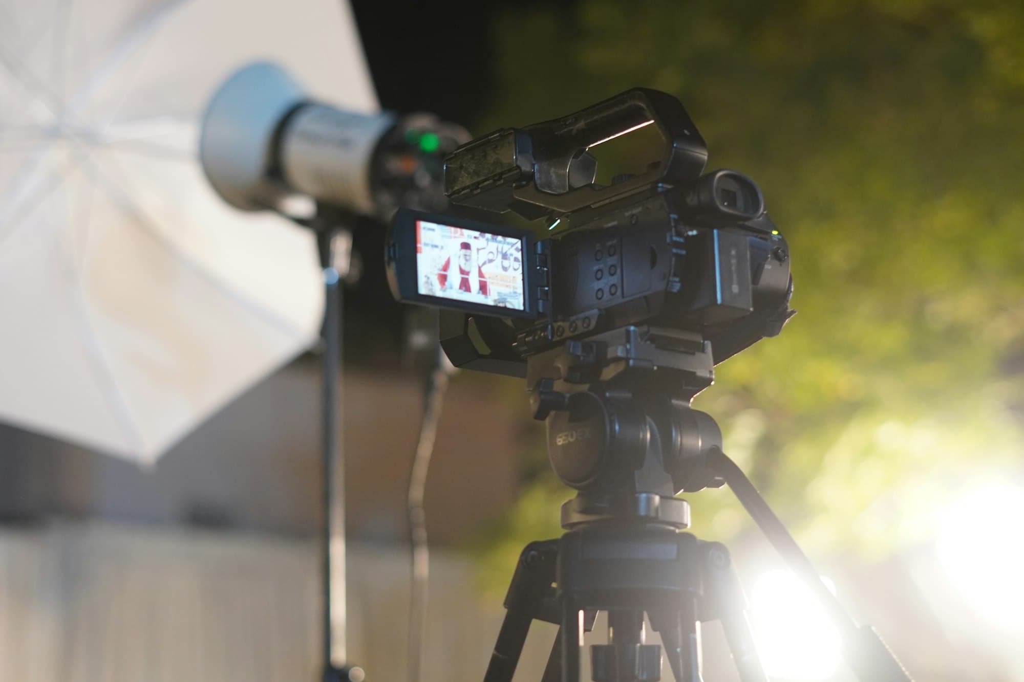 A professional video camera on a tripod beside a white umbrella light