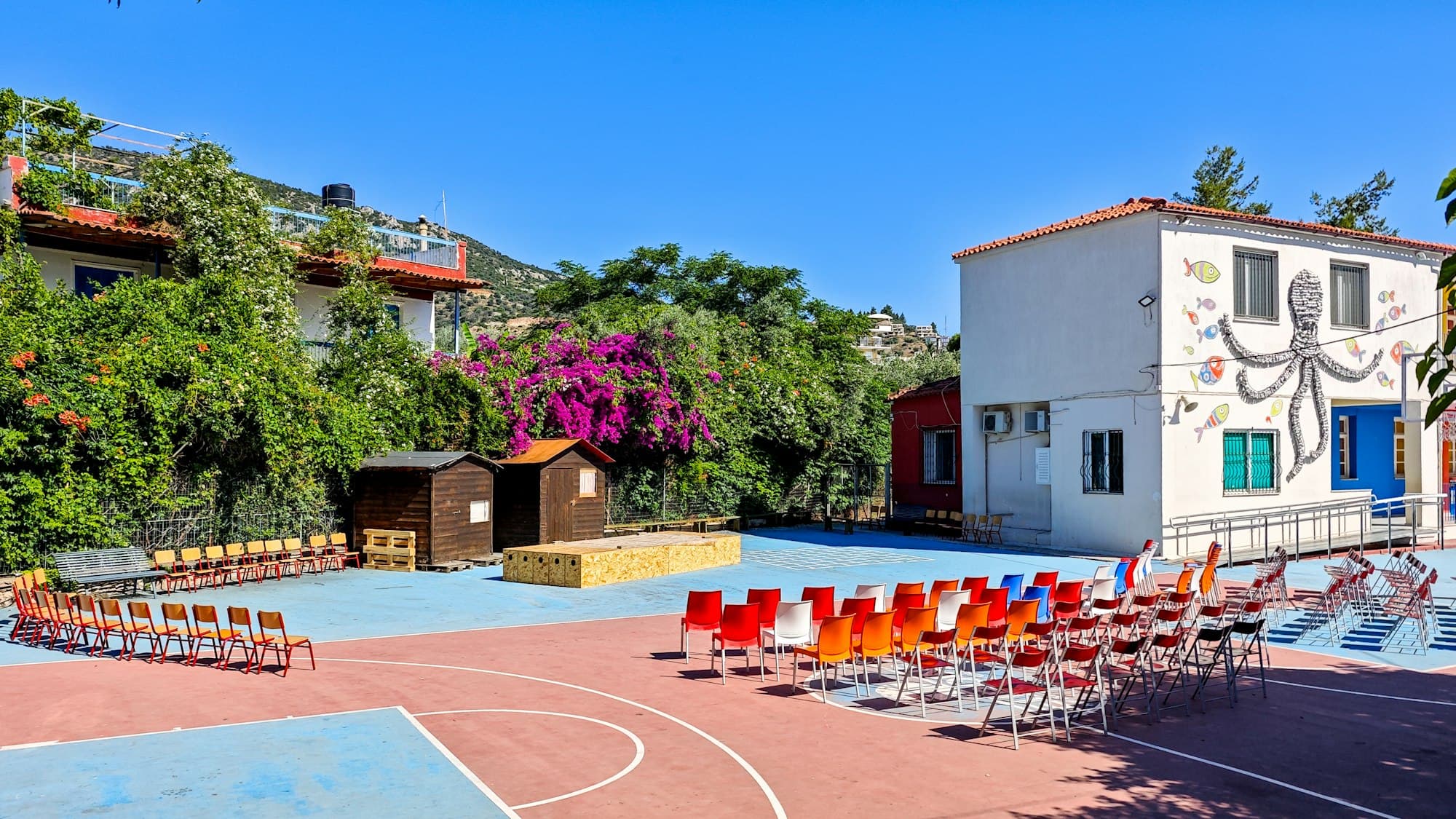 Rows of colourful chairs set out on a sunny outdoor school court with a painted mural