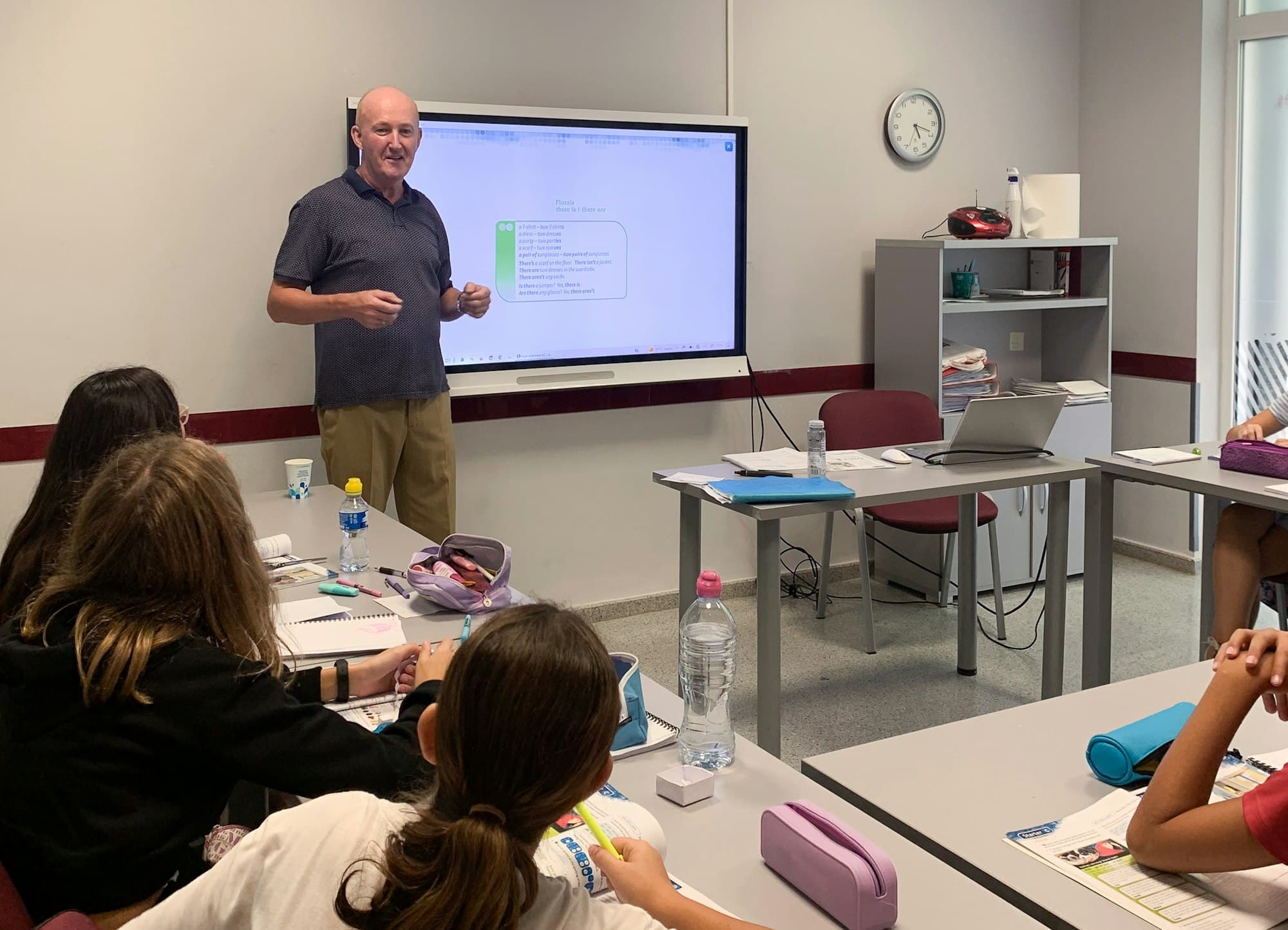 A teacher standing before a digital screen in a classroom while students sit at desks