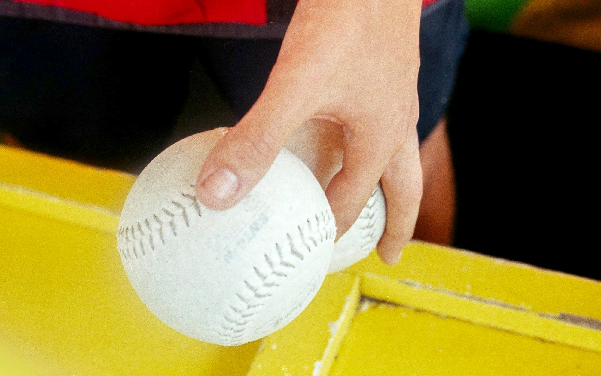 A hand holding two white baseballs over a yellow surface