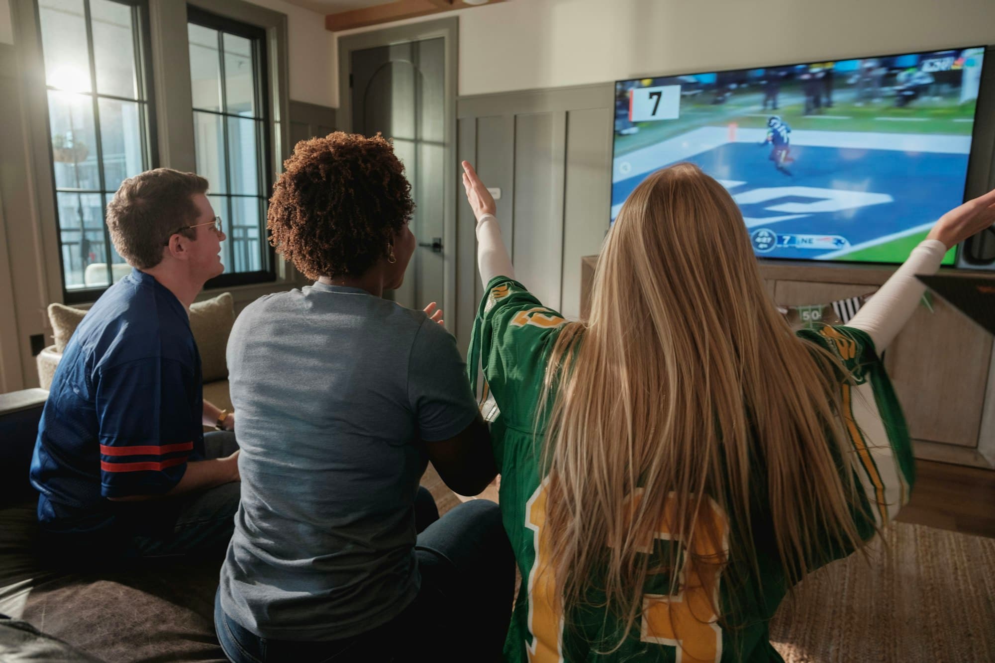 Friends cheering in a living room while watching a football game on a big TV