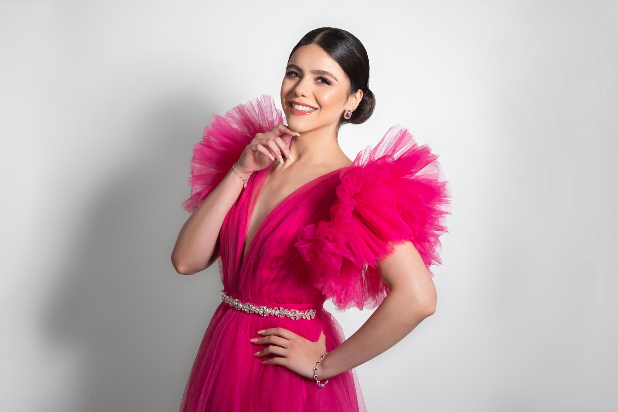 A smiling woman in a vibrant pink tulle gown with ruffled sleeves
