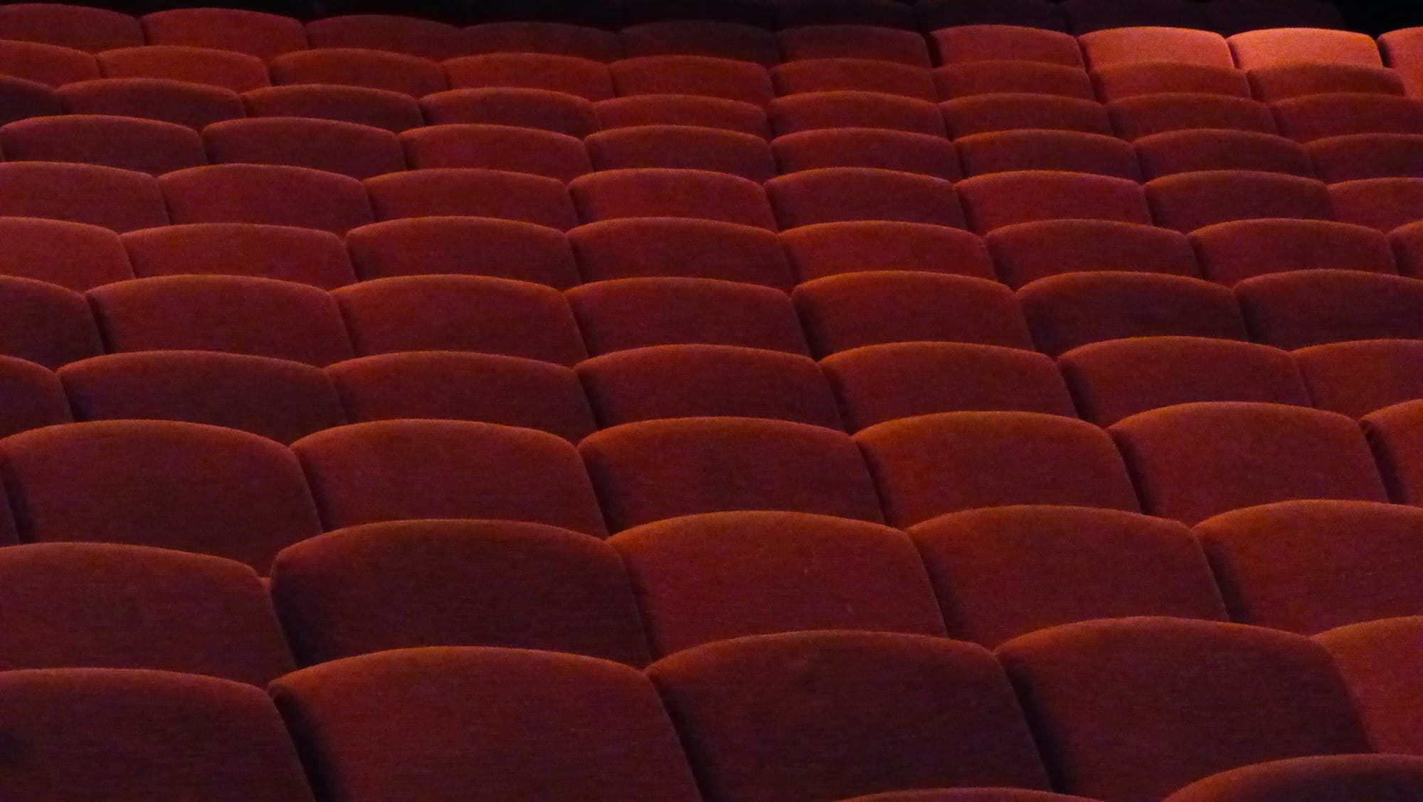 Rows of empty red velvet seats in a dimly lit auditorium