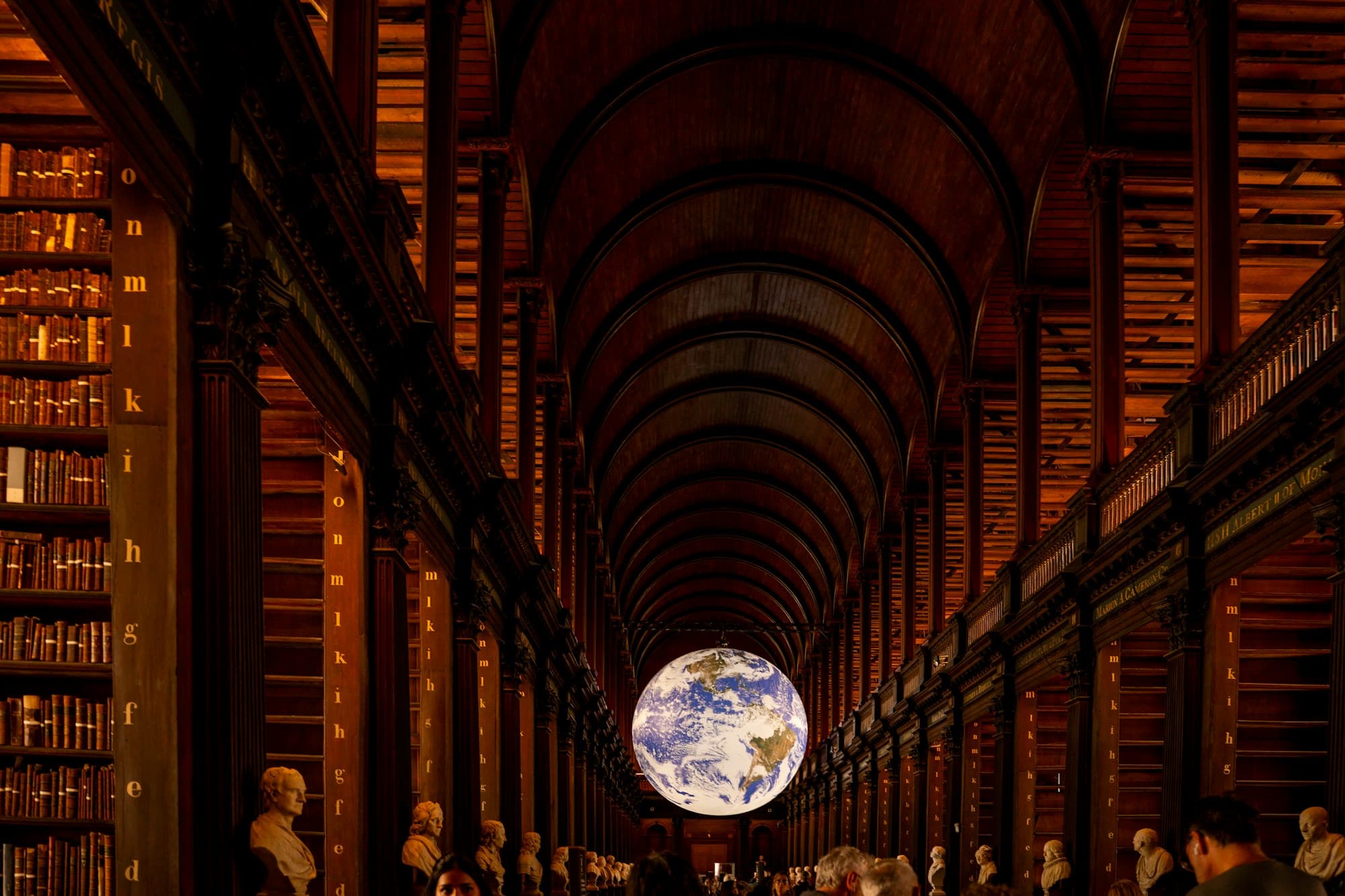 A glowing Earth globe hanging in a grand arched library hall