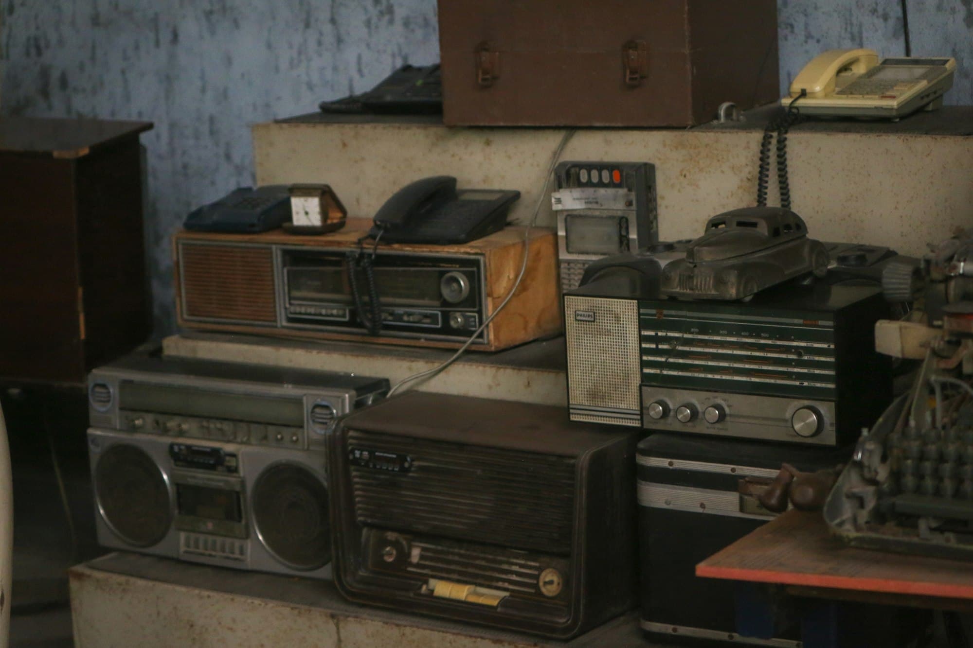 Stacked vintage radios, a boombox and old telephones on concrete steps