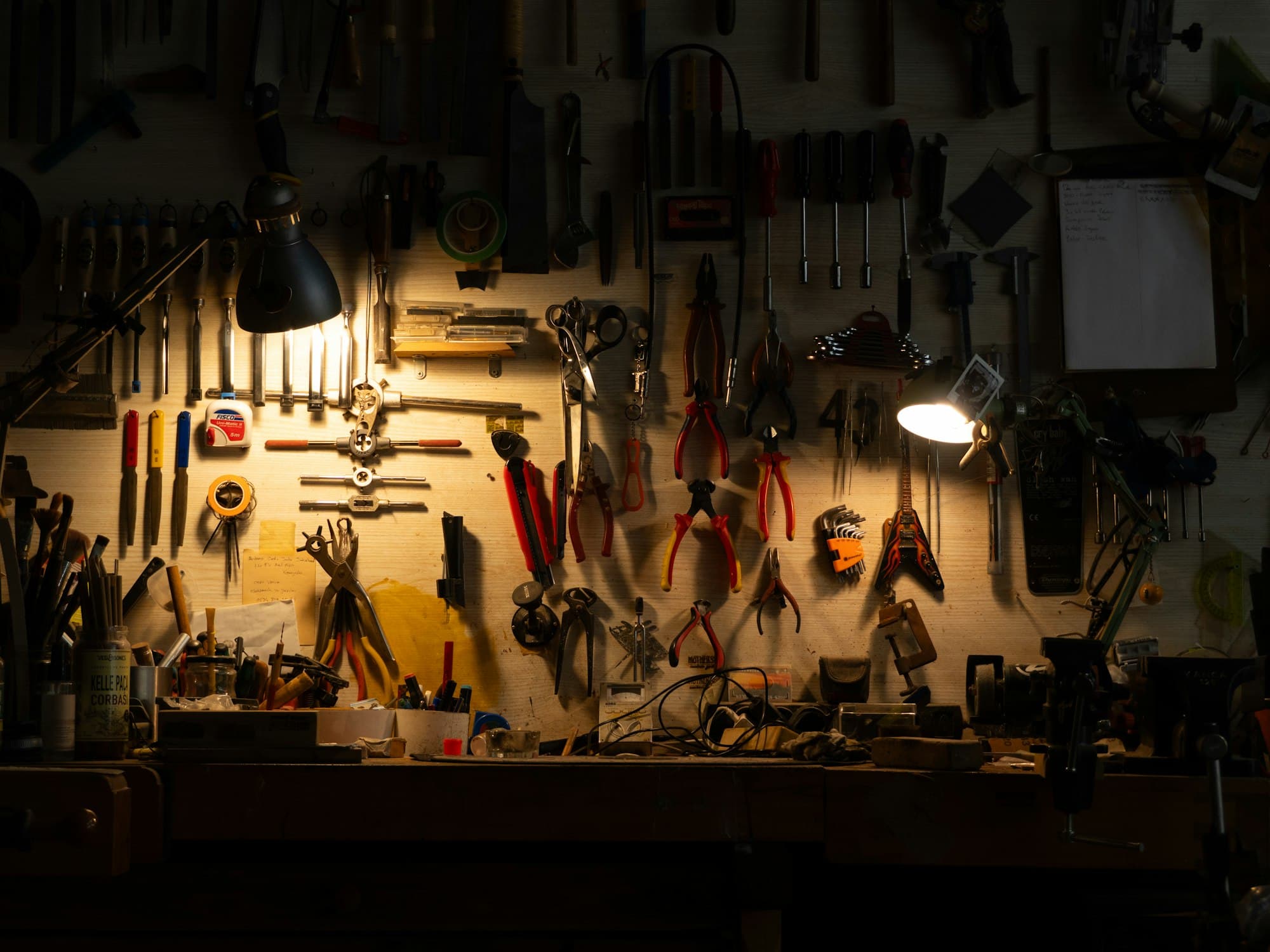 A workbench with hand tools hanging on a wall under two lamps