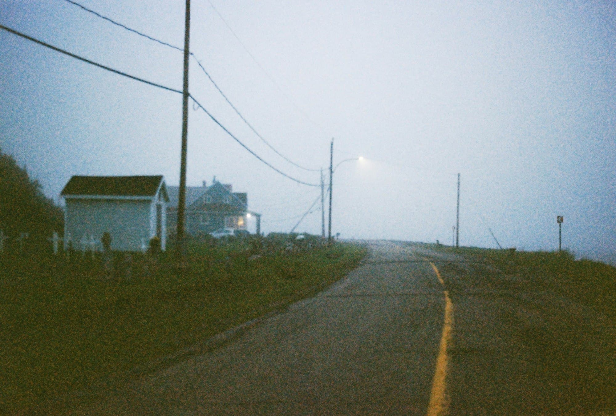 A quiet road leading past a small house in thick coastal fog at dusk