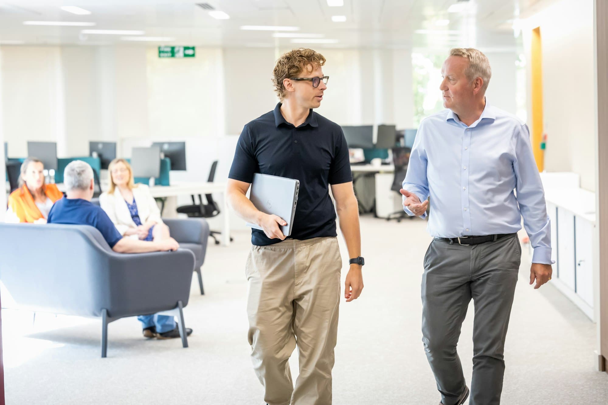Two colleagues walking and talking through a bright modern office