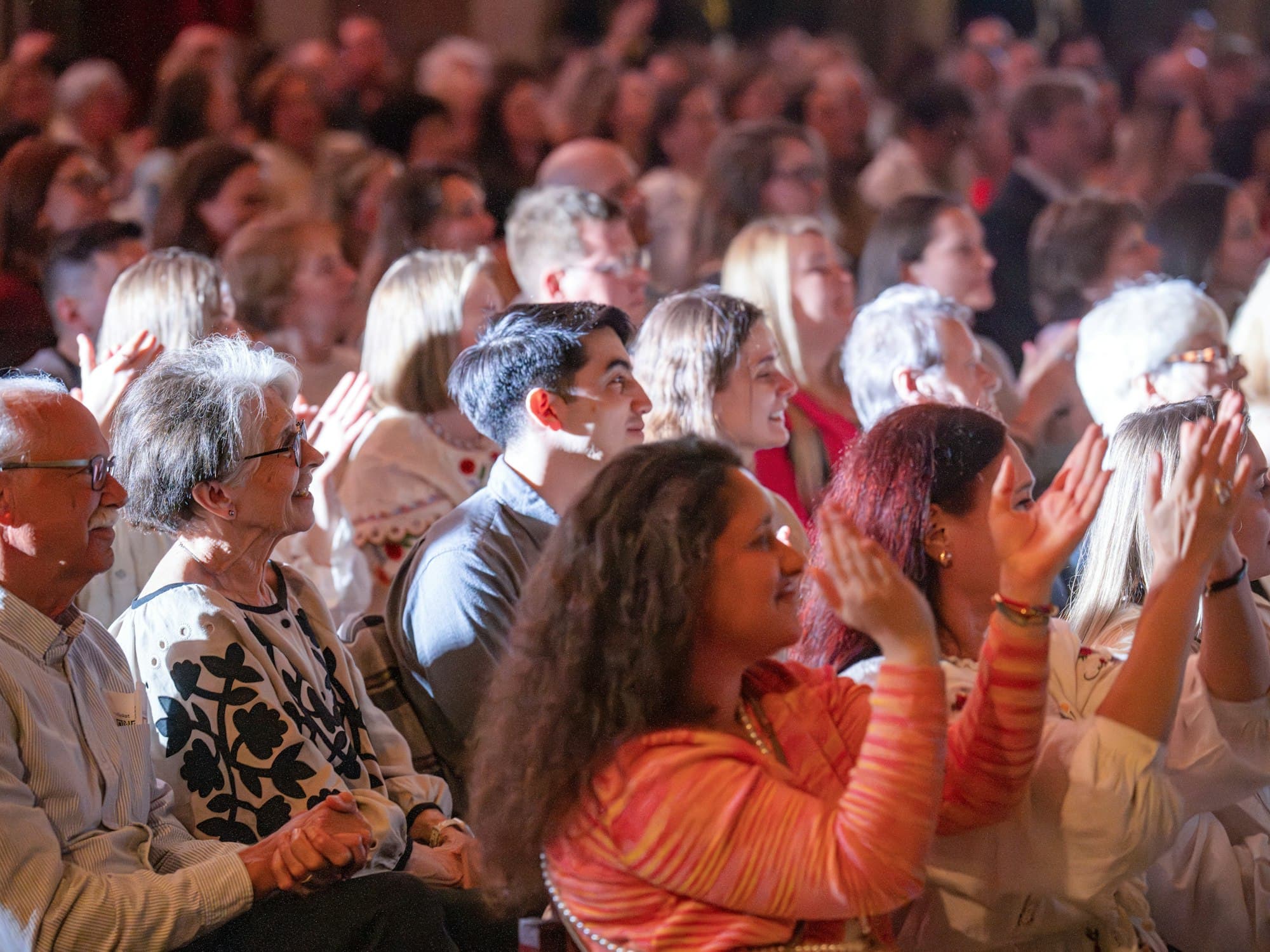 A smiling audience clapping in a dimly lit theatre