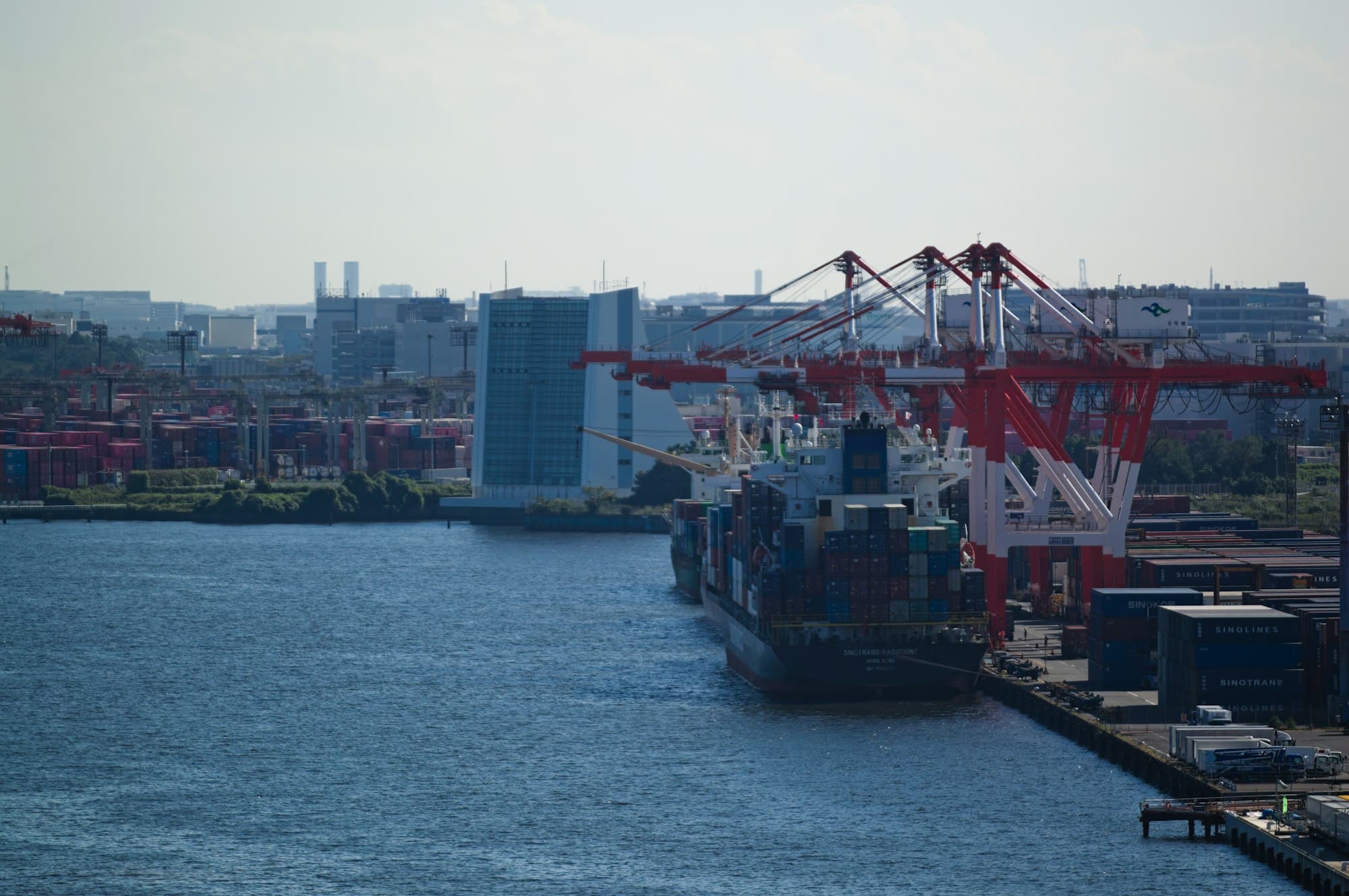 A container ship docked at an industrial port beneath red cranes