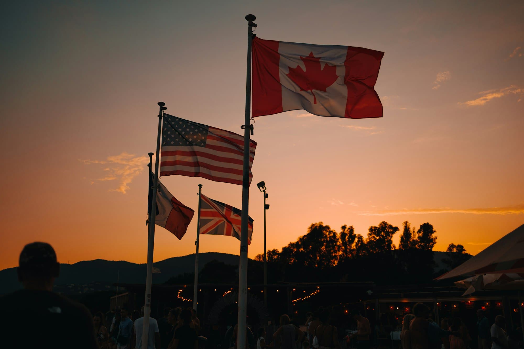 Flags of Canada, the United States and the United Kingdom against an orange sunset sky