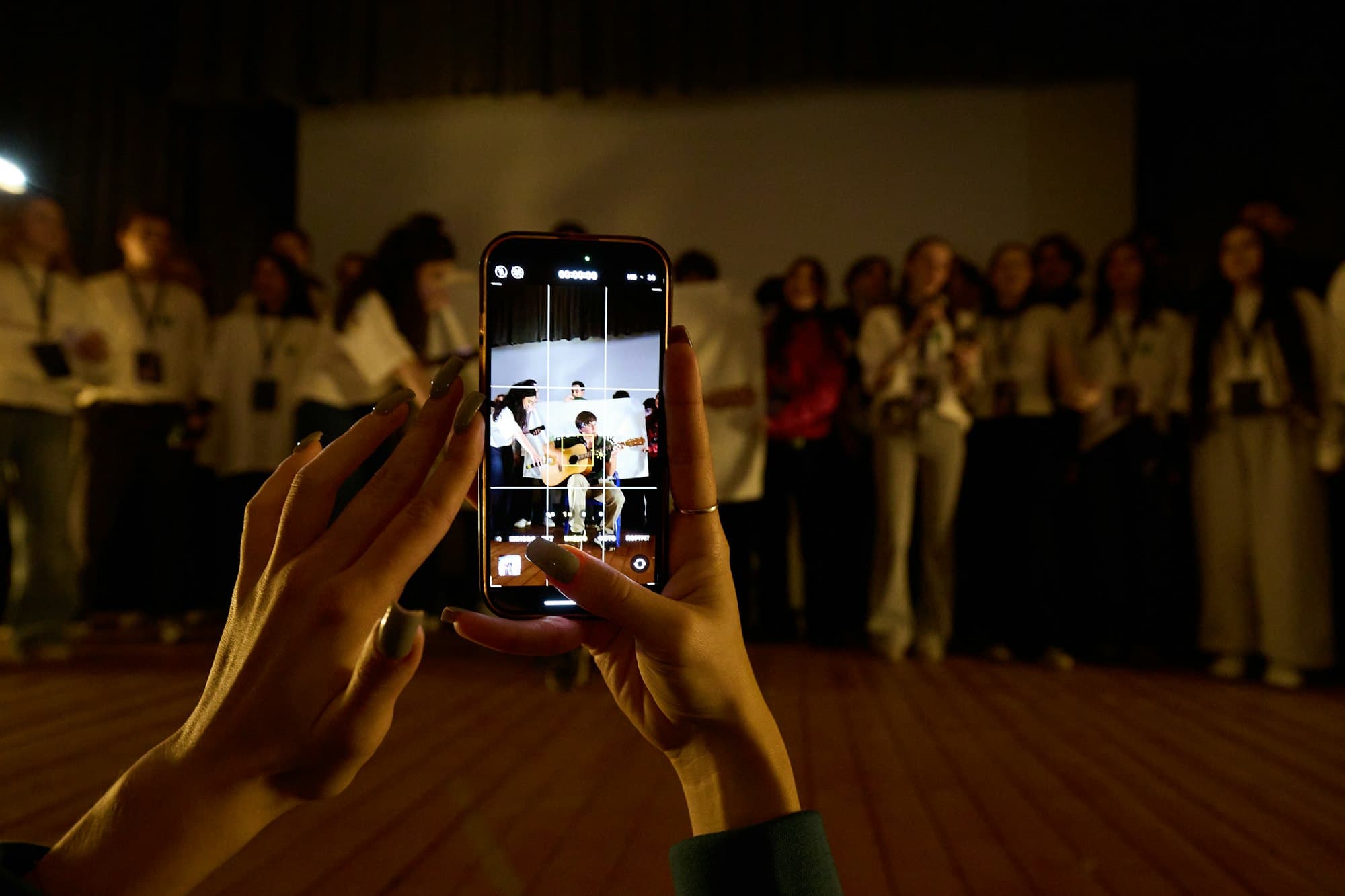 Hands holding a smartphone to record a musician performing on stage