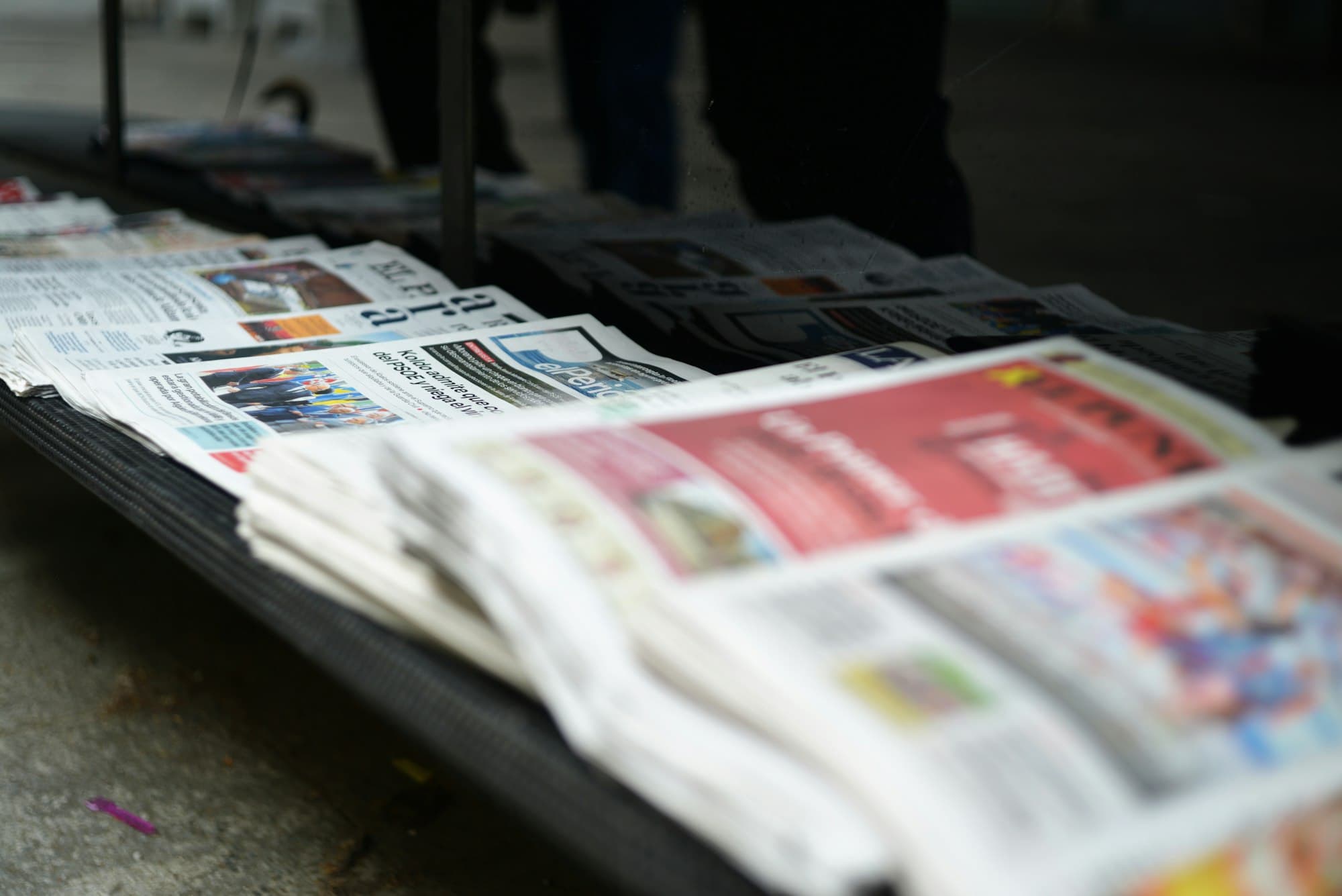 A stack of newspapers laid out on a metal rack, softly blurred