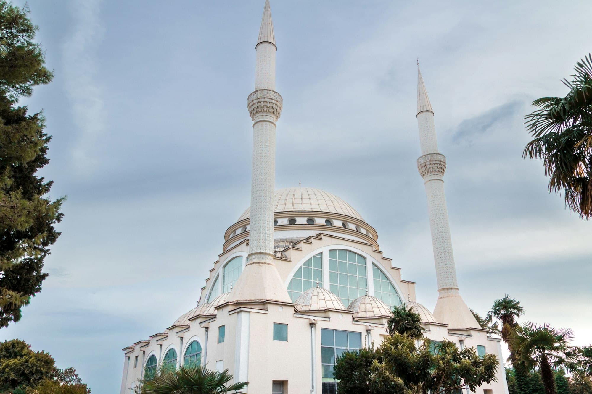 A white mosque with a large dome and two tall minarets among palm trees