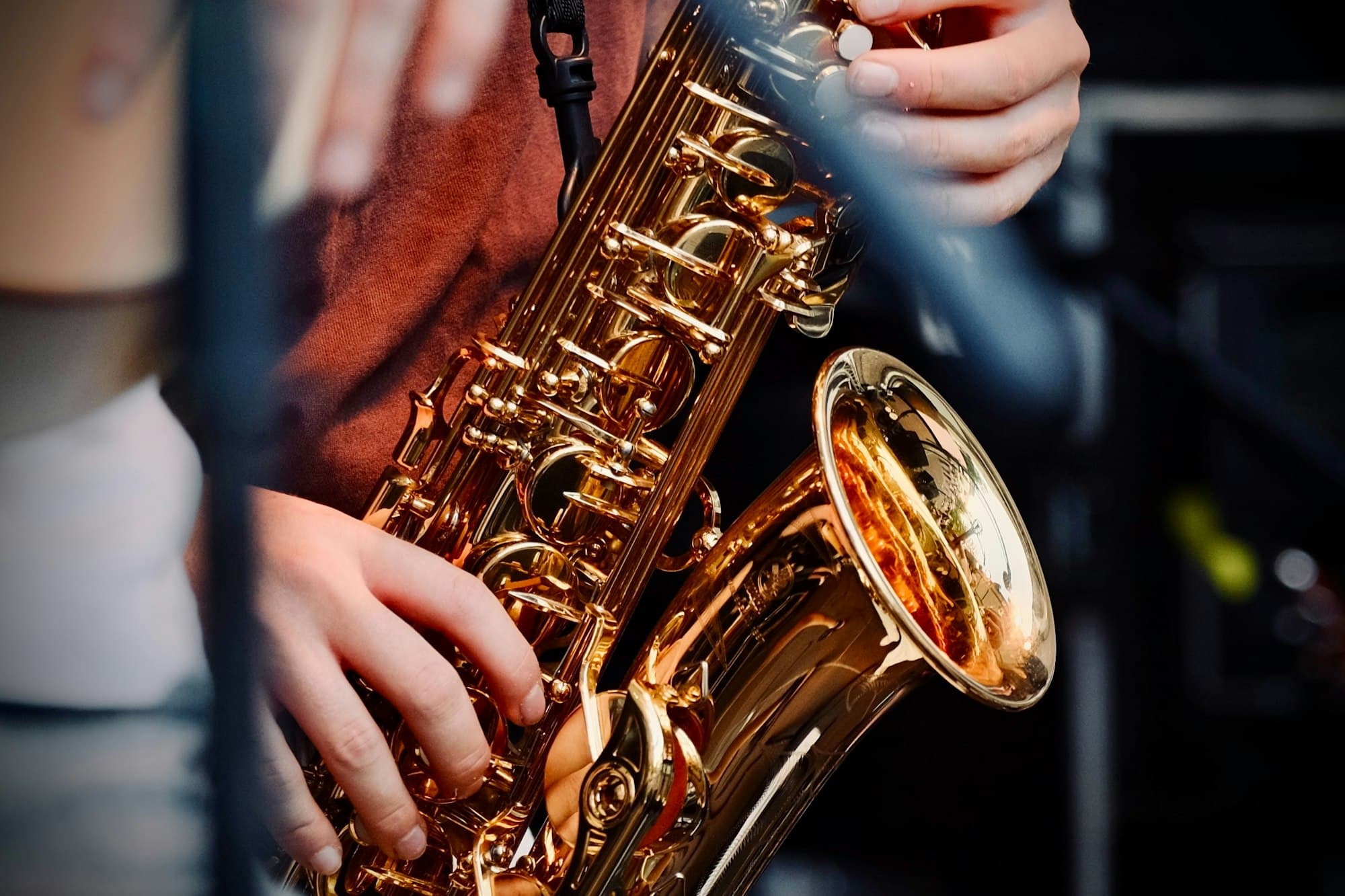 Close-up of a musician's hands on a shiny gold saxophone on a dark stage