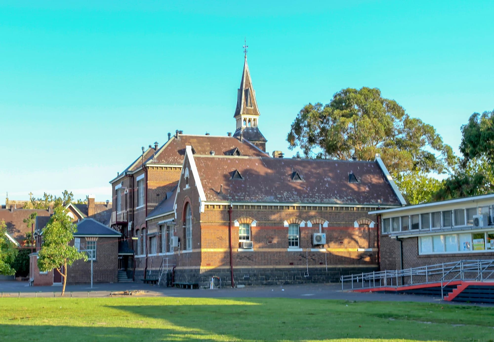 A historic red brick school building with a steeple under a clear blue sky