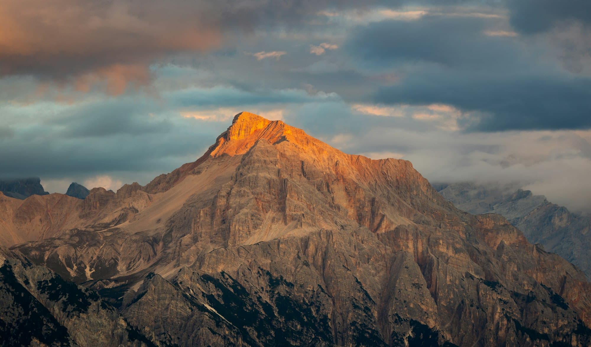 A rocky mountain summit lit by warm golden light against a cloudy sky