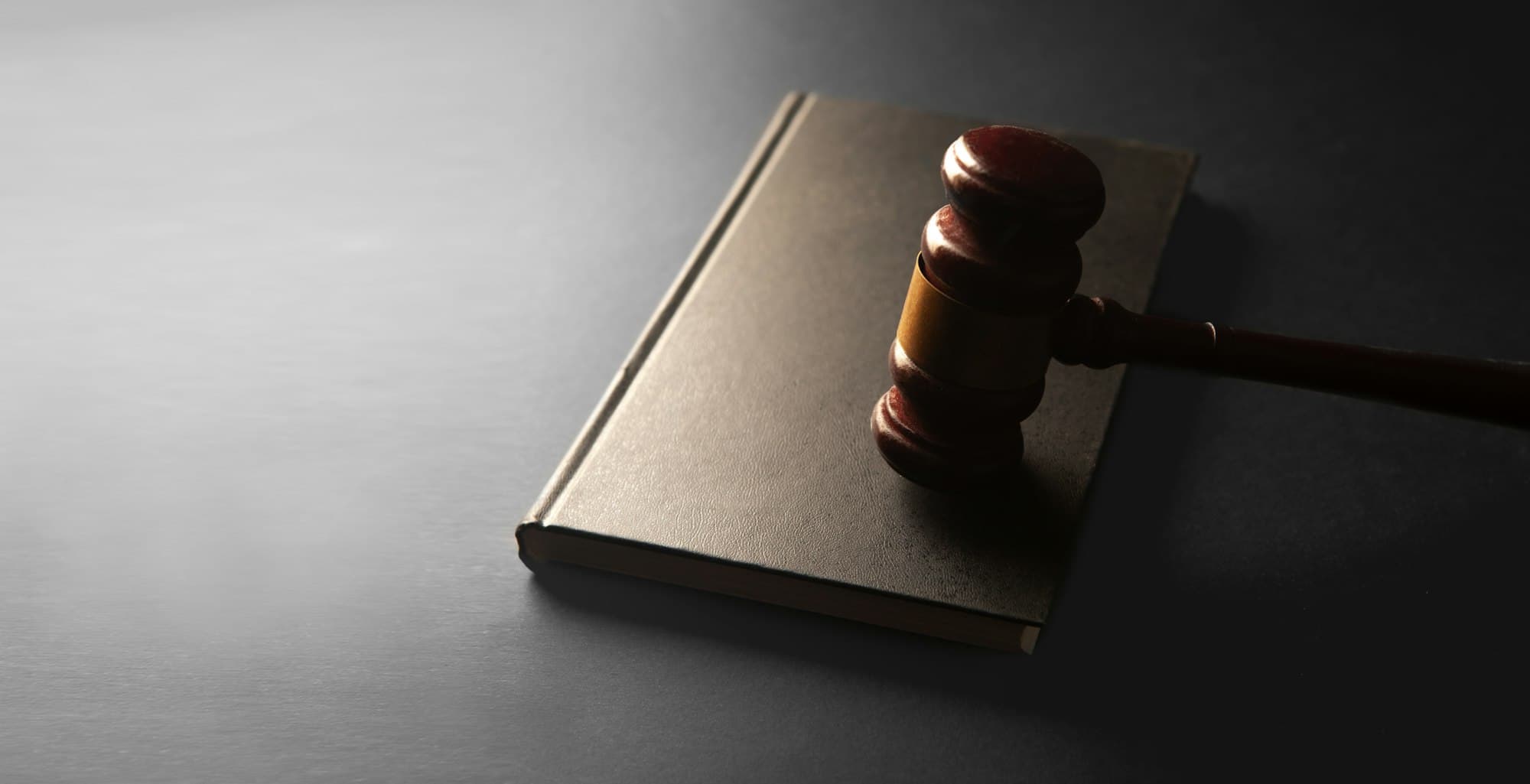 A wooden gavel resting on a closed book on a dark surface