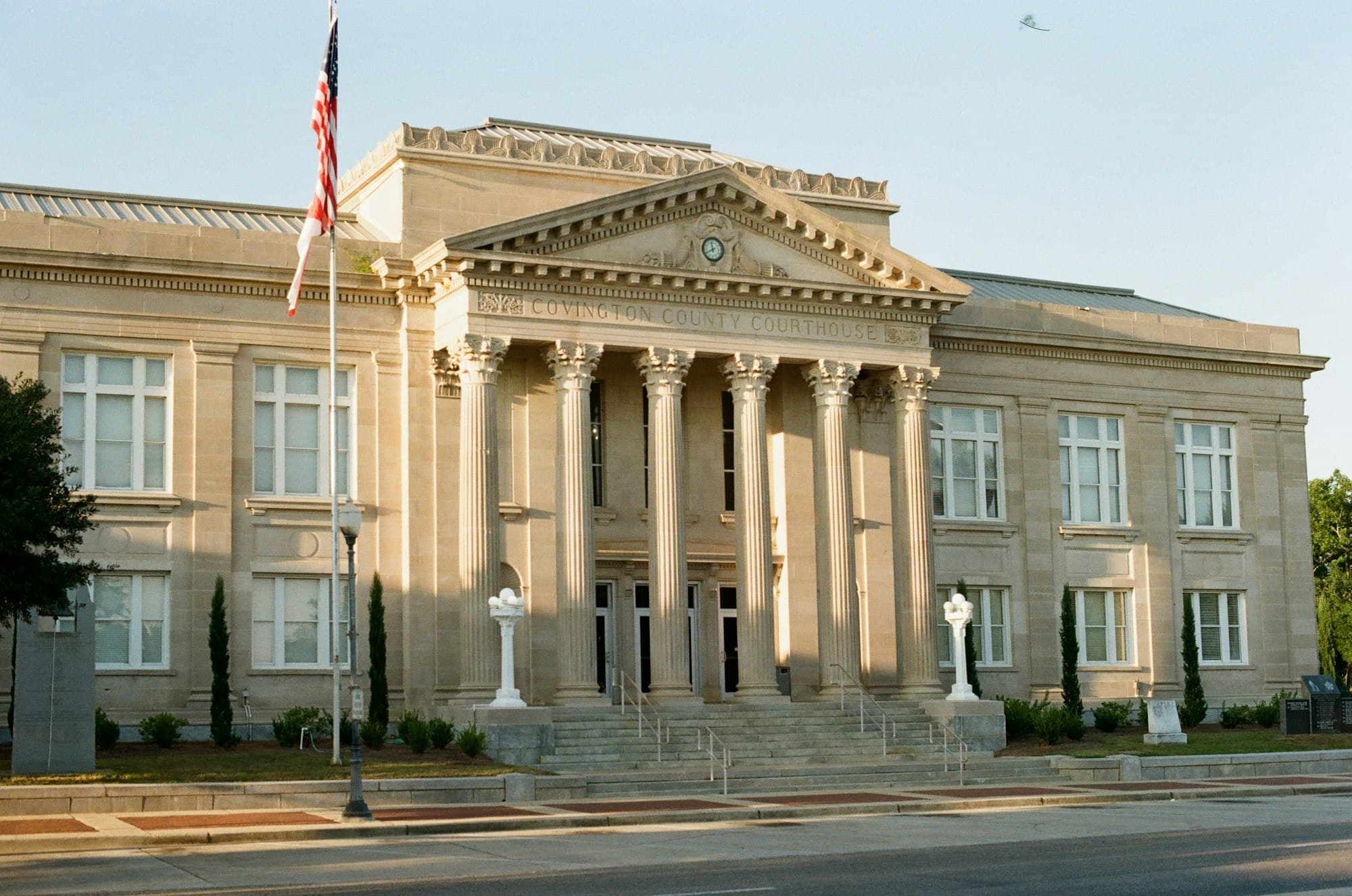 A neoclassical courthouse with tall columns and an American flag in warm evening light