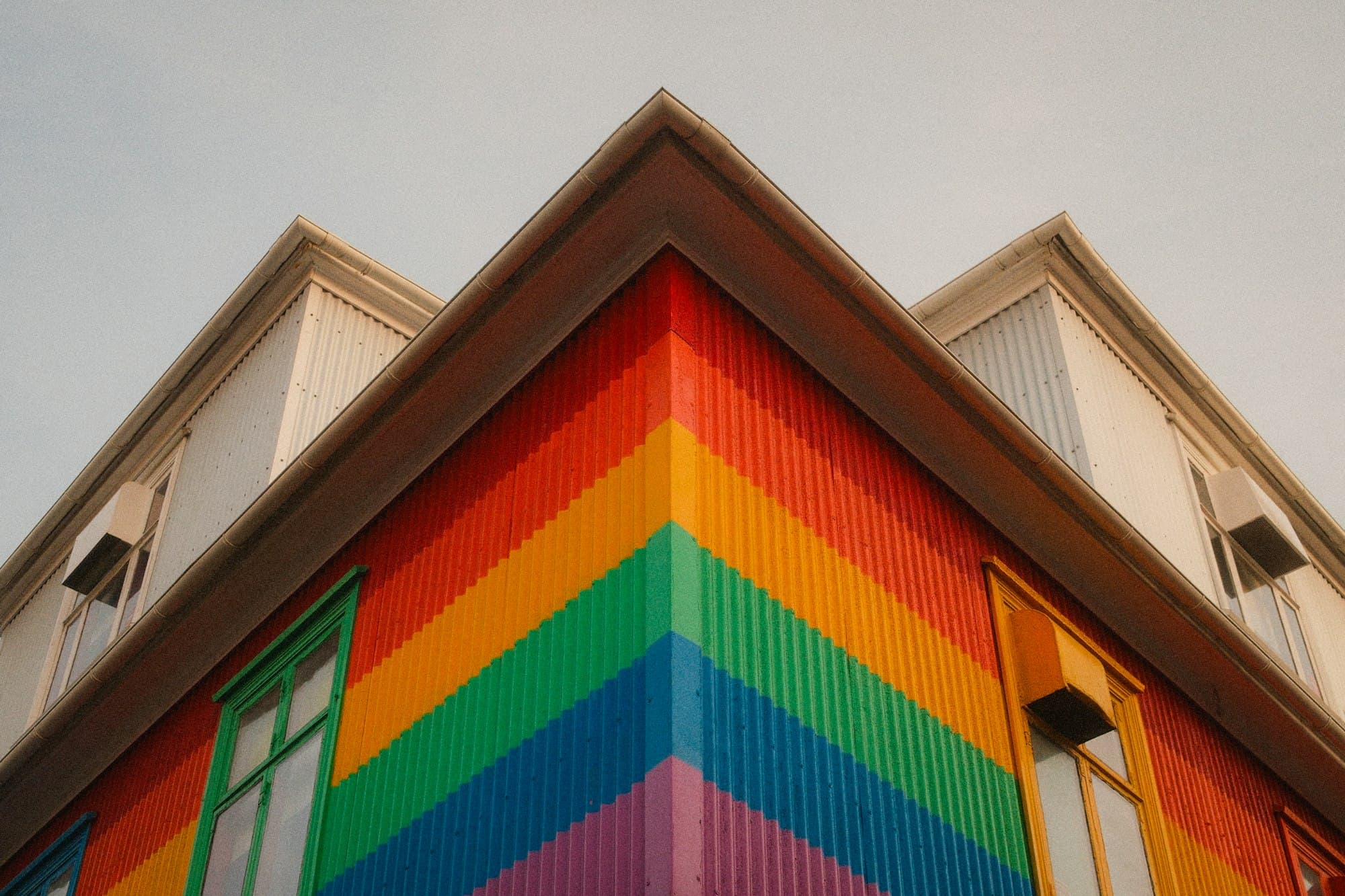 The corner of a building painted in bright rainbow stripes against a pale sky
