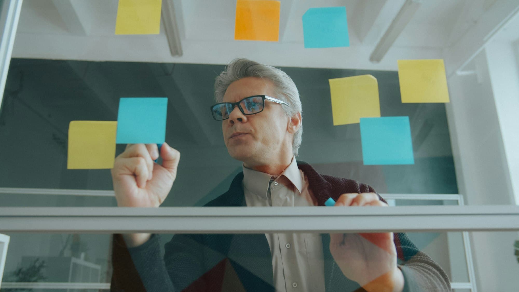 A man with glasses placing colourful sticky notes on a glass wall