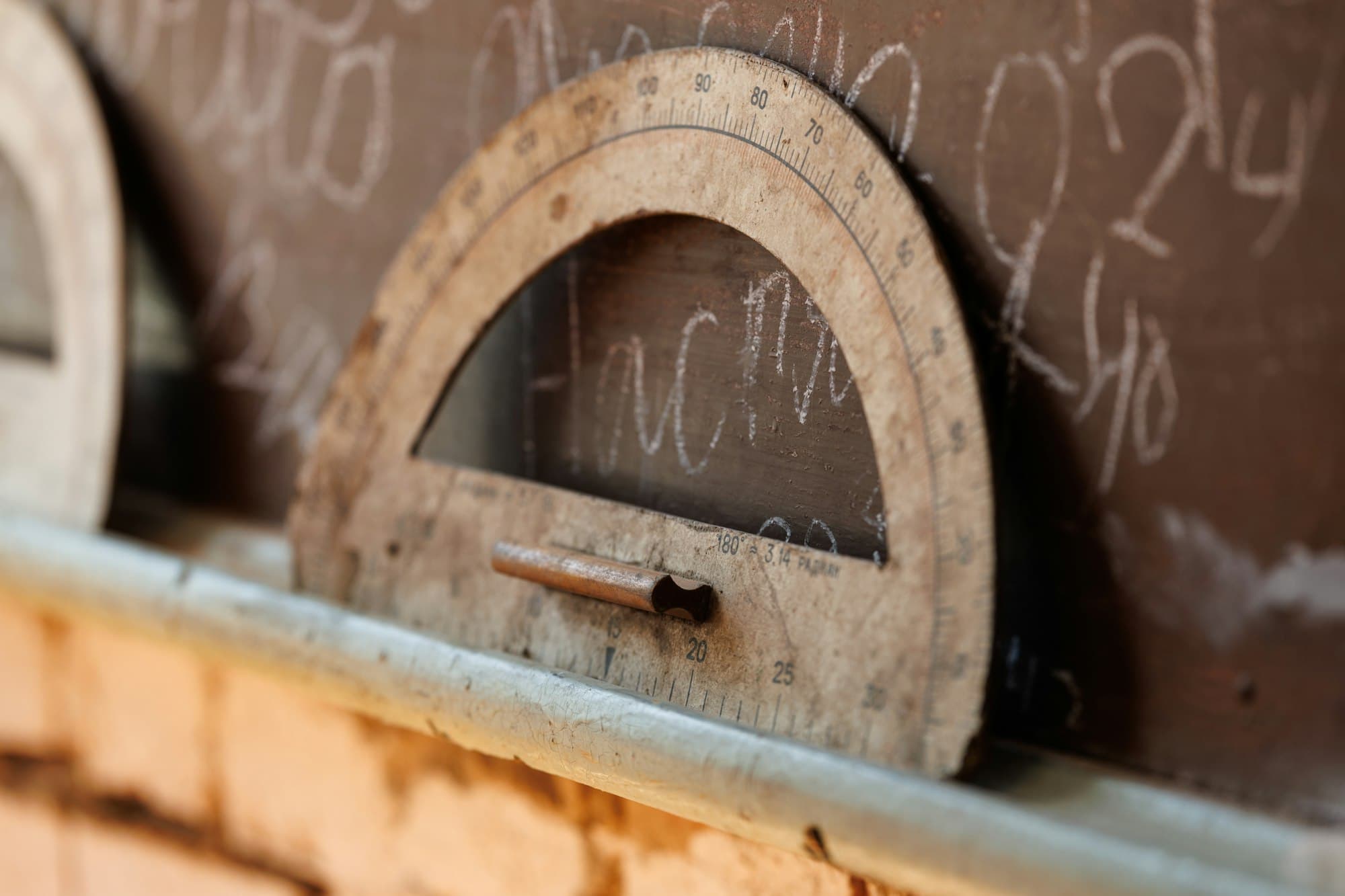 A wooden teaching protractor leaning against a chalkboard marked with numbers