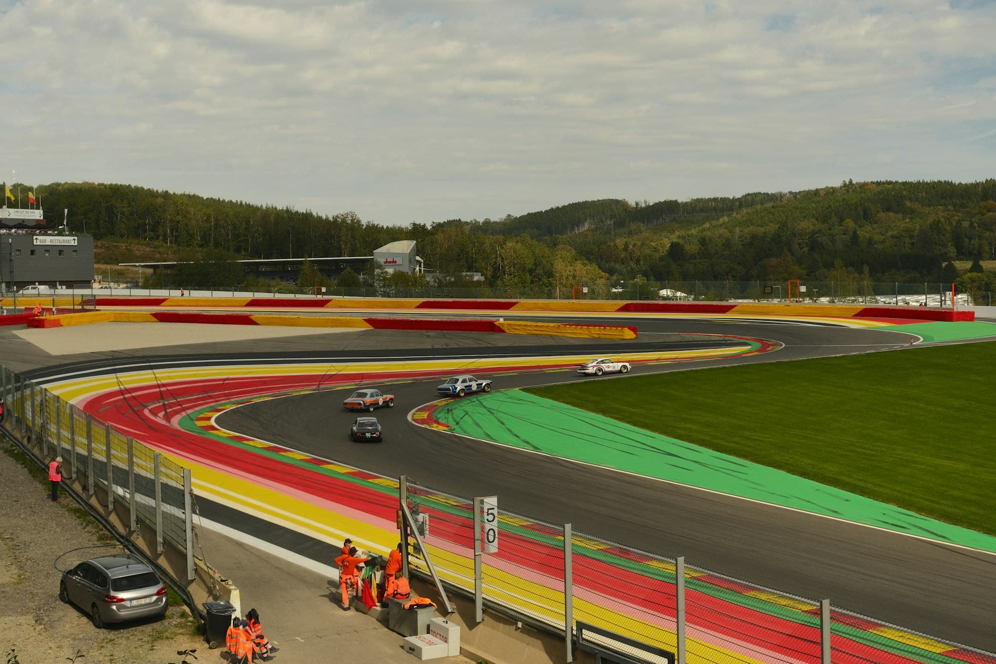 Vintage race cars cornering on a colourful kerbed circuit at Spa-Francorchamps