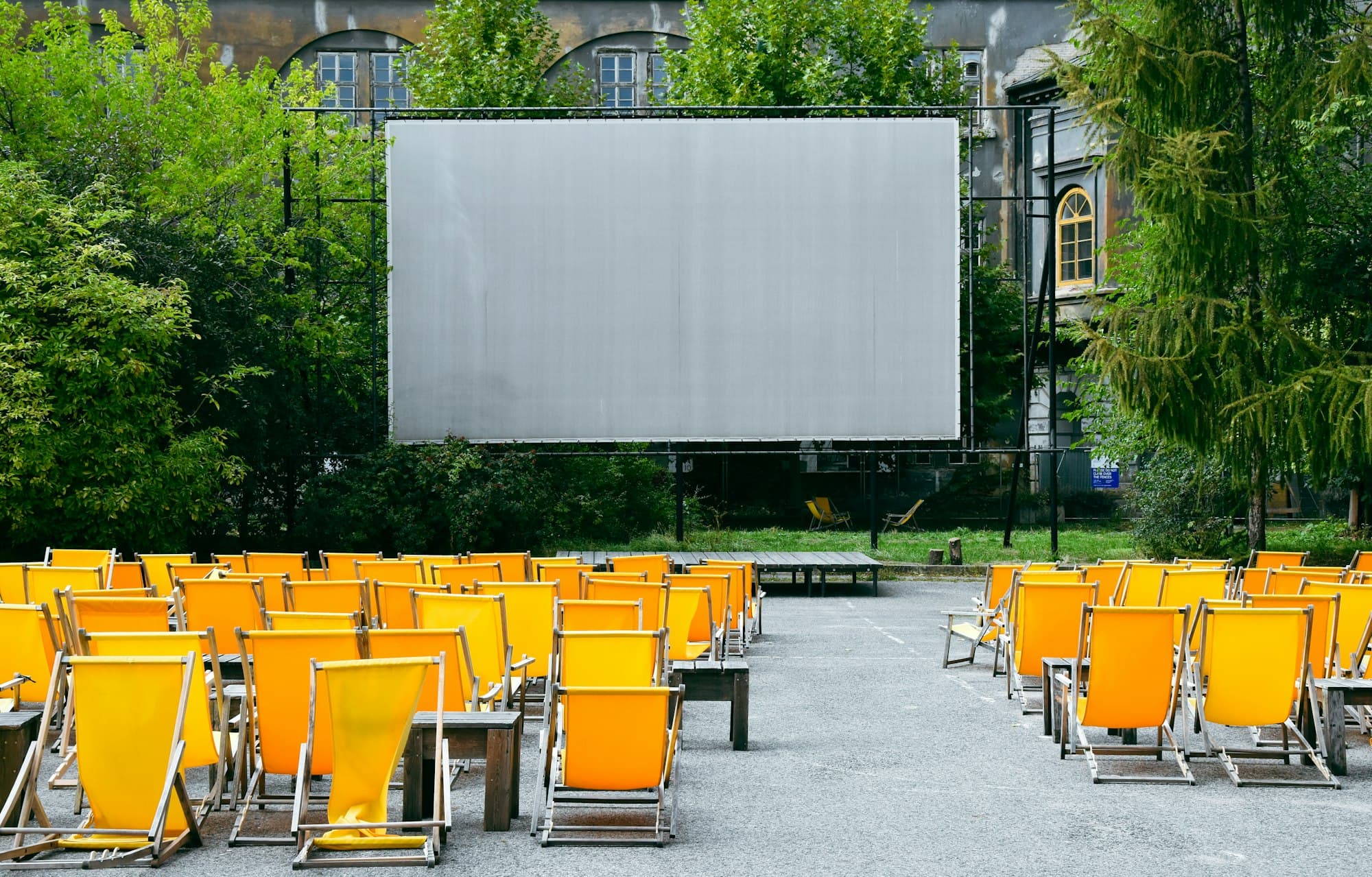 Rows of yellow deck chairs facing a large outdoor cinema screen in a courtyard