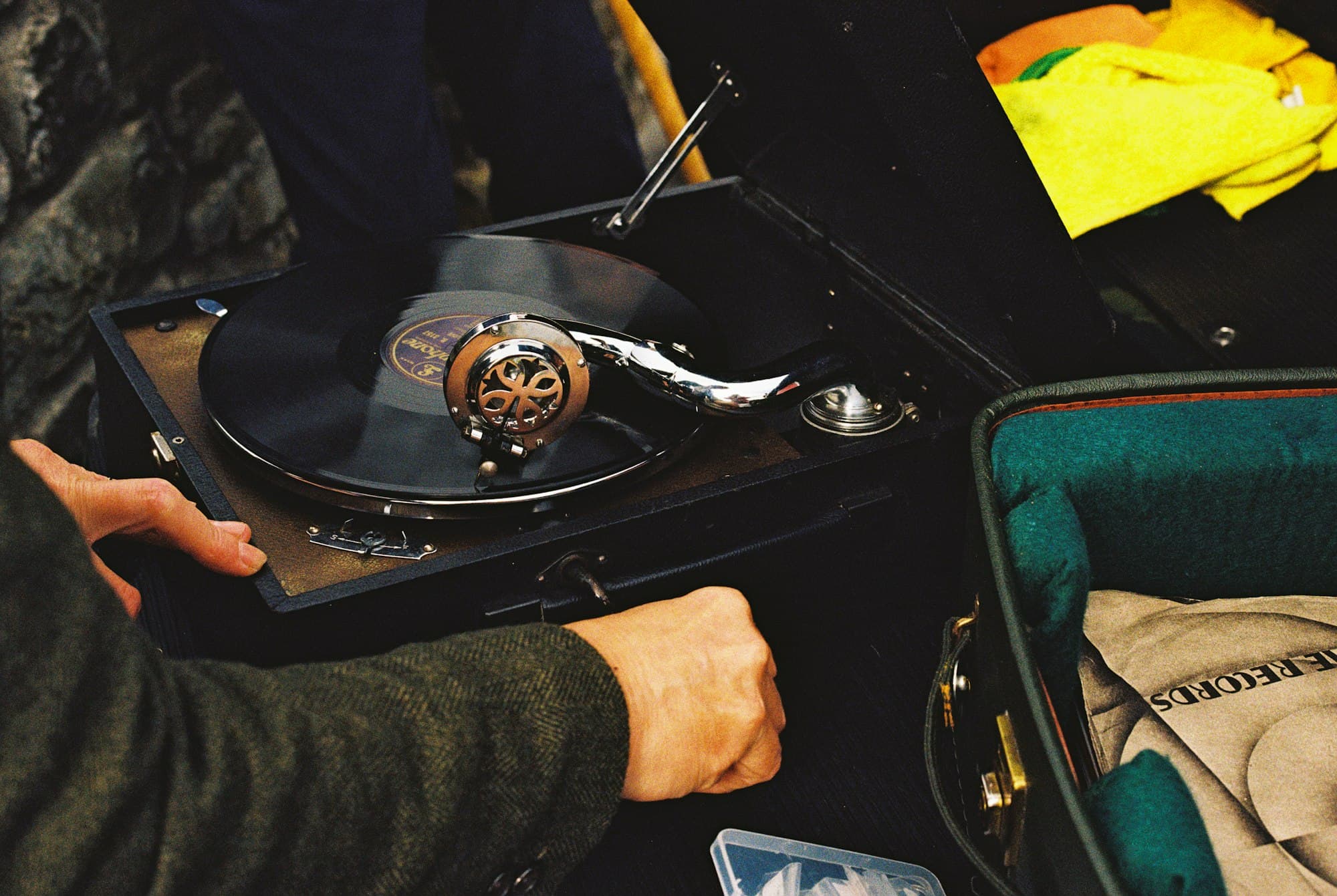 A hand adjusting a vintage portable record player with a black vinyl disc spinning
